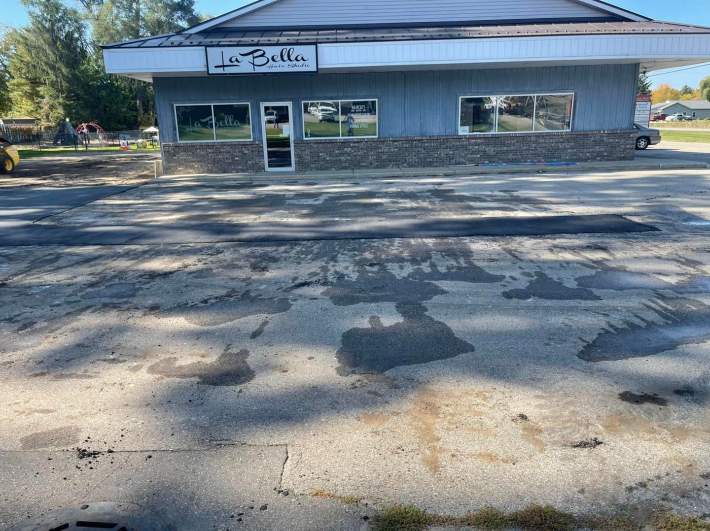 Small gray storefront with a sign and empty parking lot in front, seen from across the street