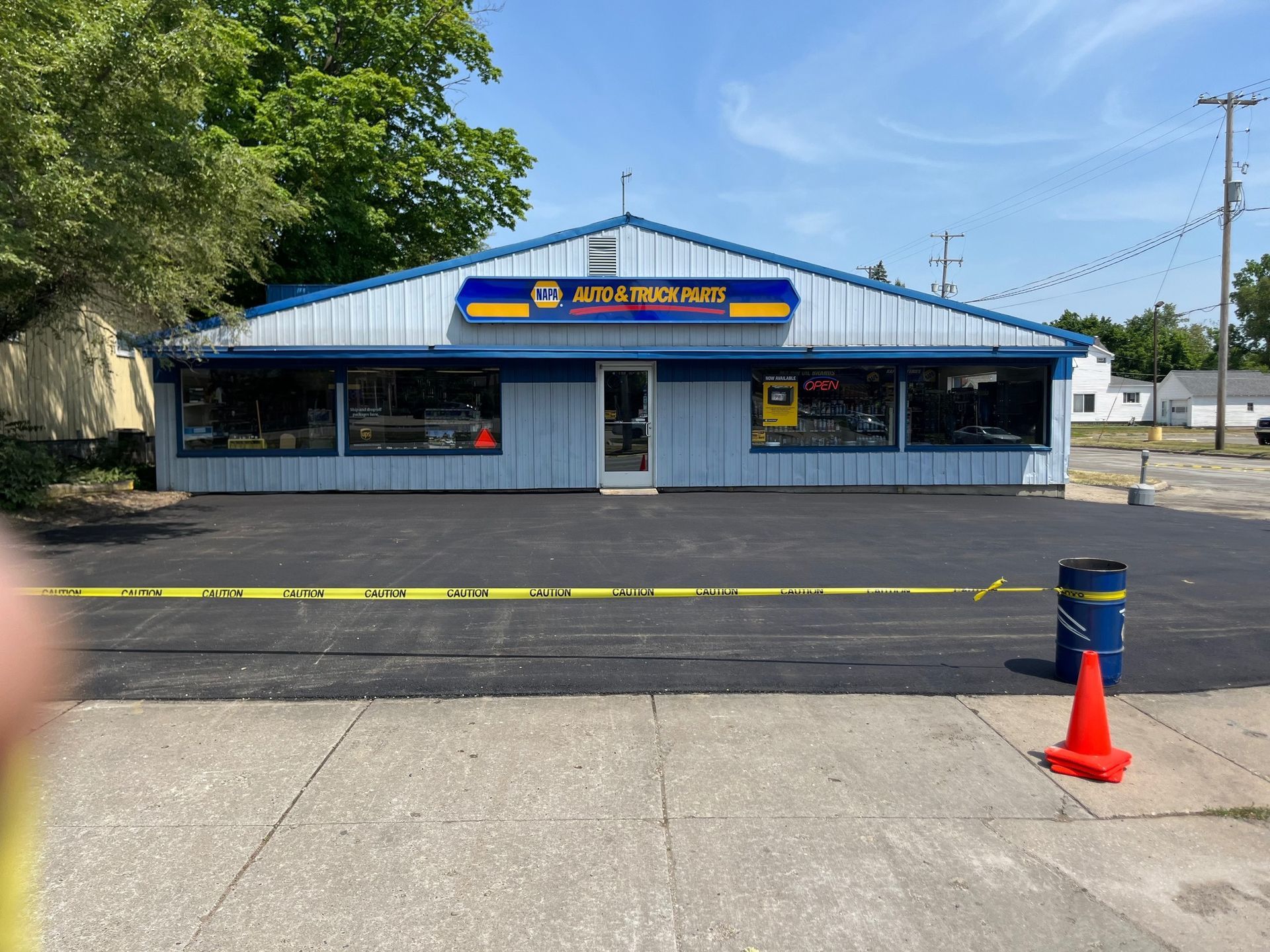 Auto repair shop storefront with blue roof and parking lot, viewed from across the street
