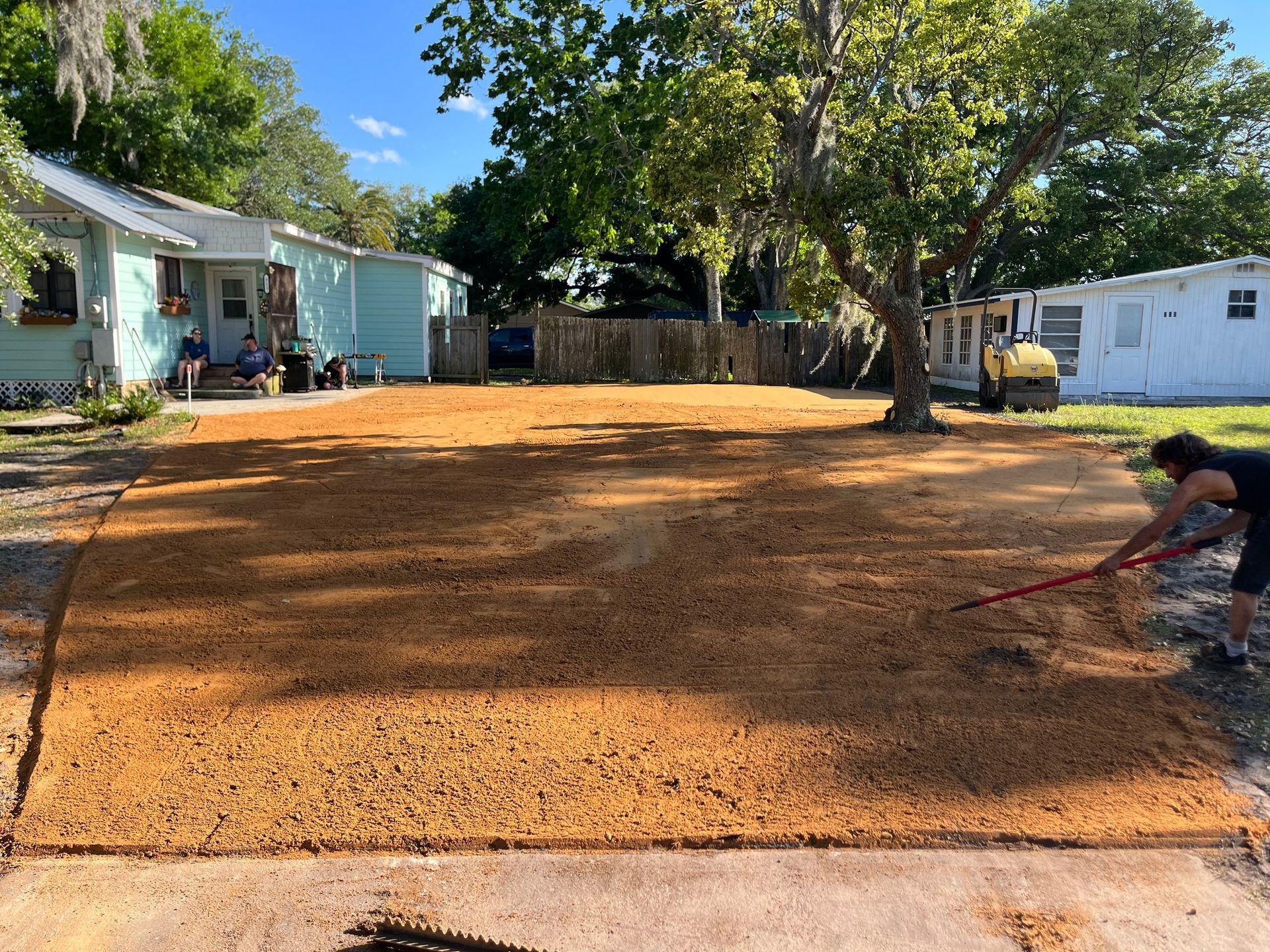 Freshly spread tan mulch in a residential yard, with a person raking on the right side.