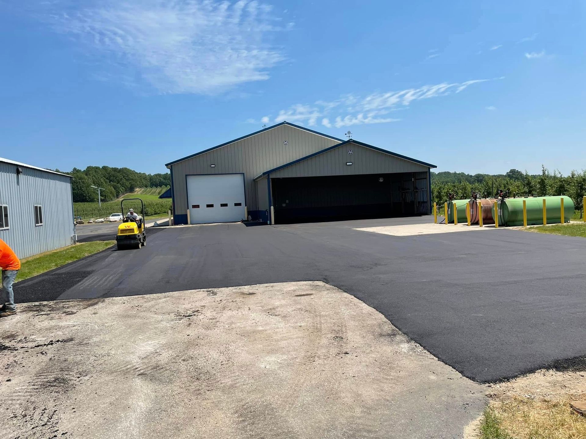 Industrial building with fresh blacktop driveway, gravel foreground, and parked equipment on a sunny day