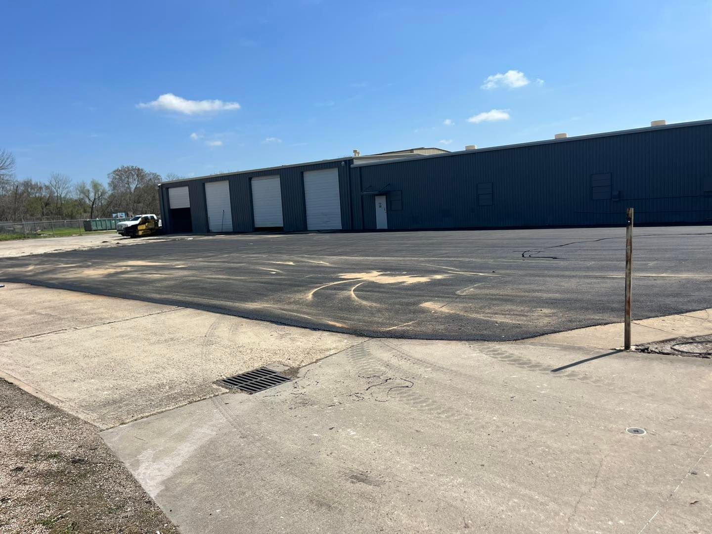 Empty industrial parking lot beside a long blue warehouse under a clear sky