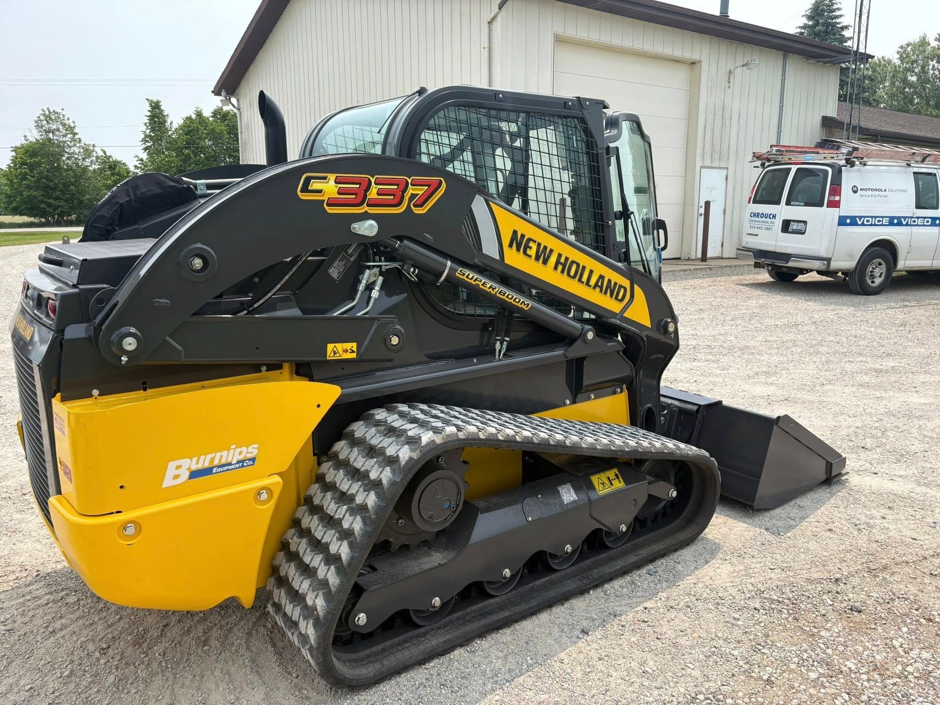 Yellow-and-black tracked Bobcat compact loader parked on gravel outside a building