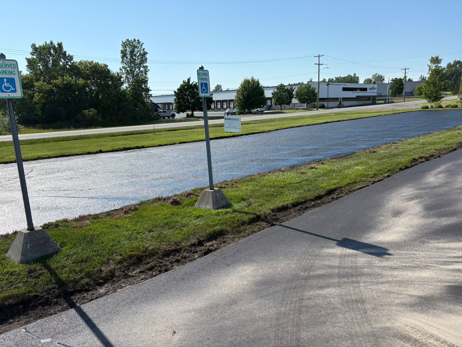 Parking lot edge beside a flooded roadway, with grassy median and blue handicap signs under a clear sky.