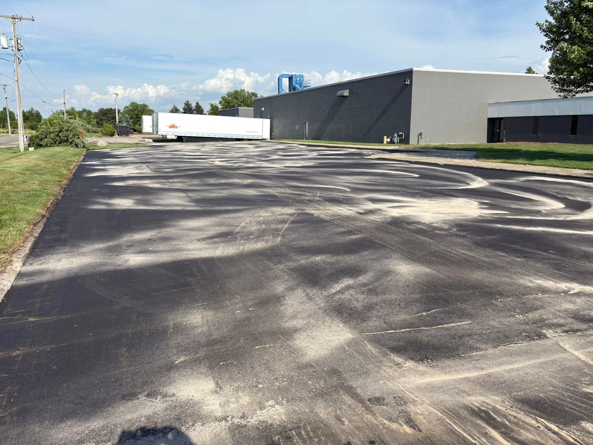Cracked asphalt parking lot beside a gray industrial building on a sunny day