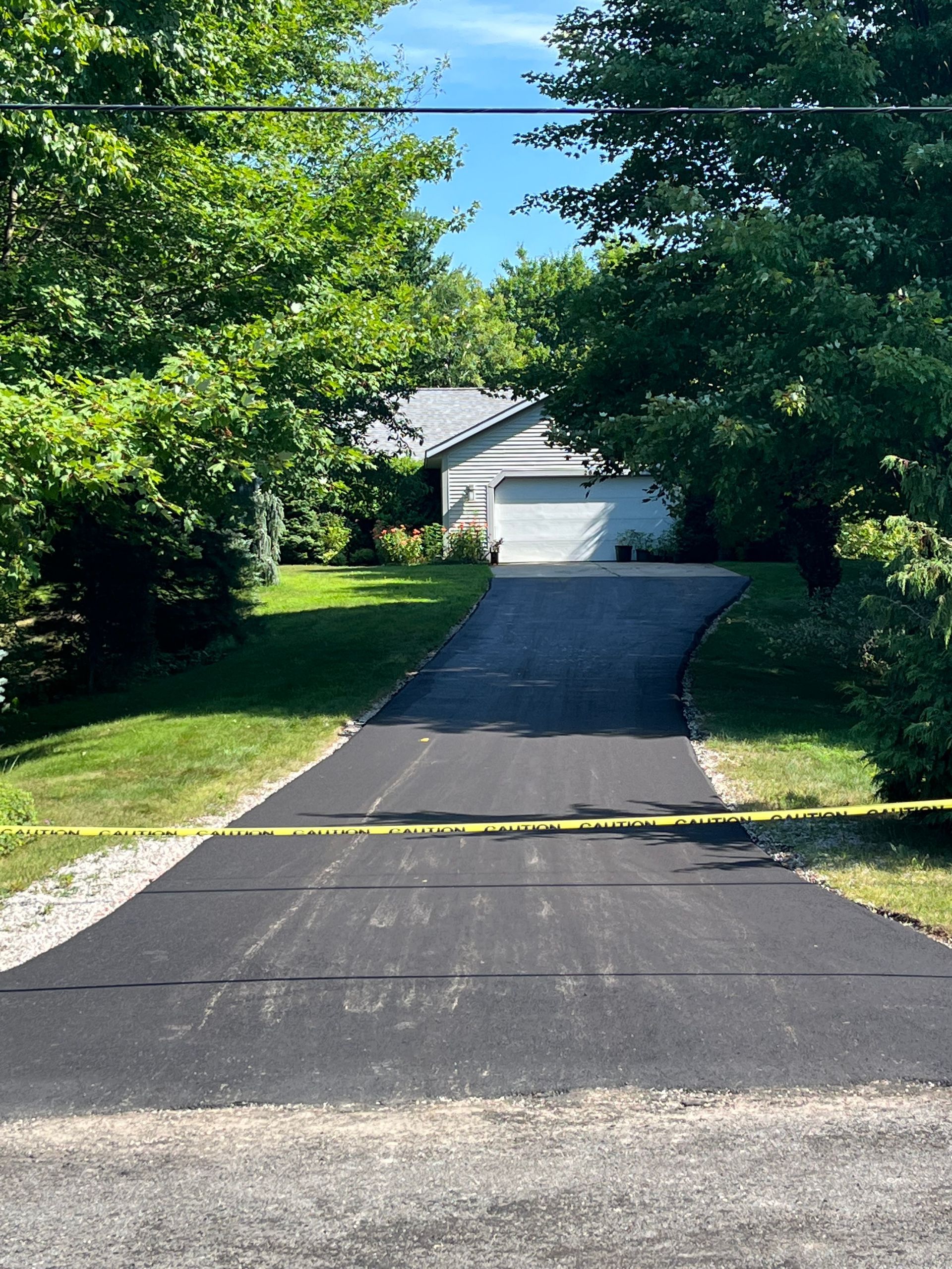 Tree-lined driveway leading to a white garage, with a yellow caution tape across the entrance.