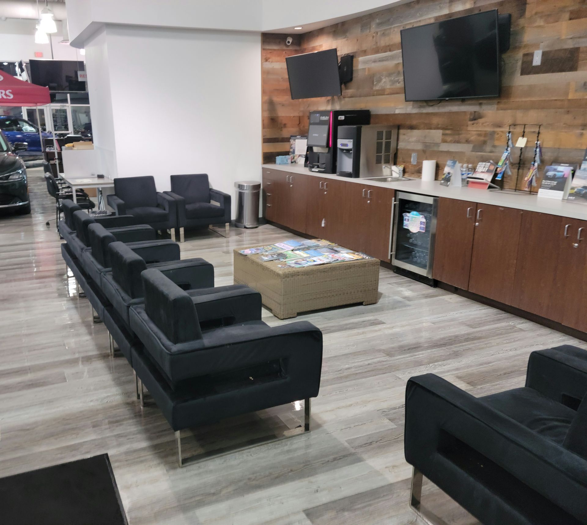 Modern lounge area with black sofas, coffee table, wood floor, and a beverage counter with TVs.