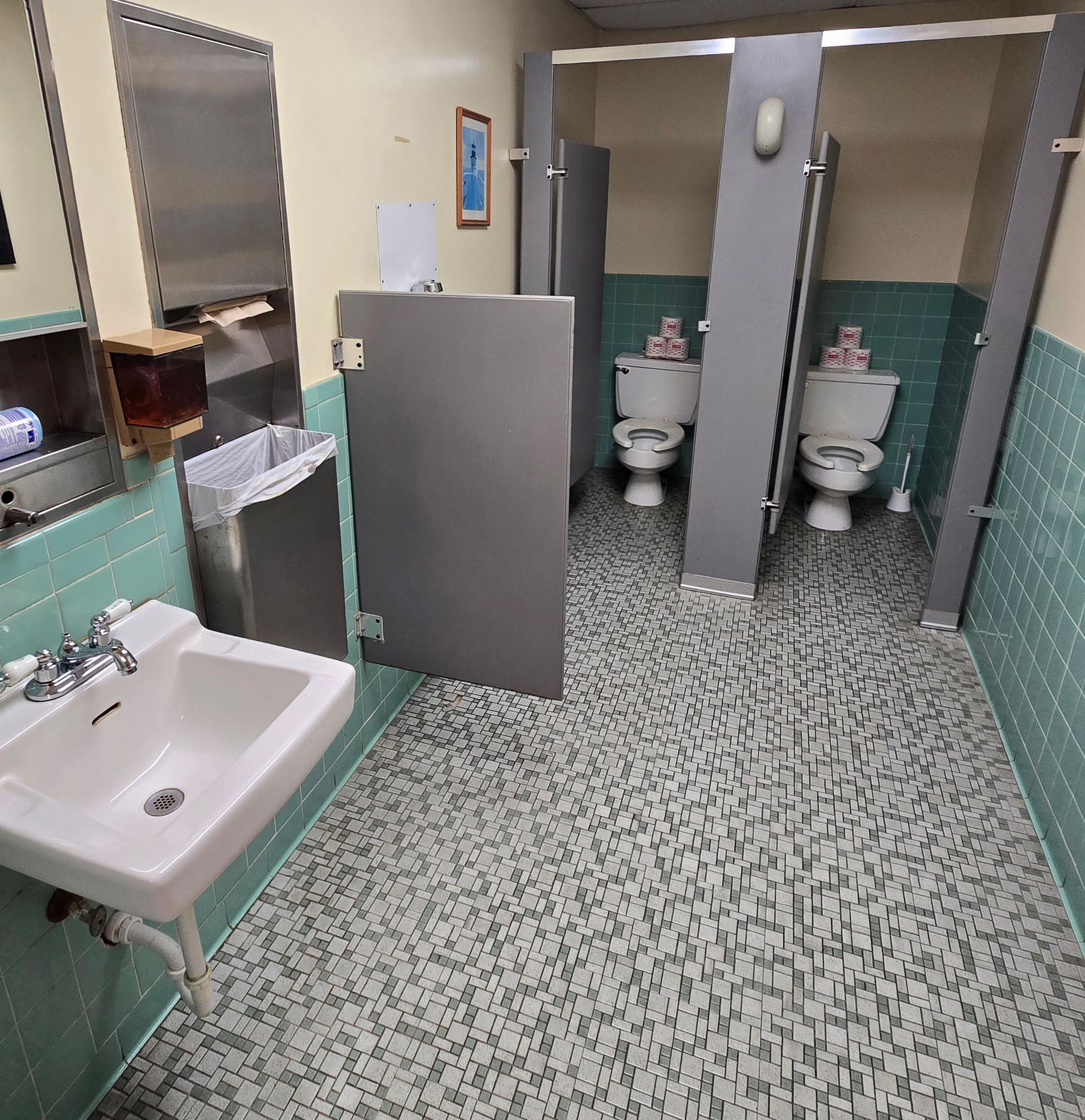 Public restroom with stalls, sink, and speckled tile floor.