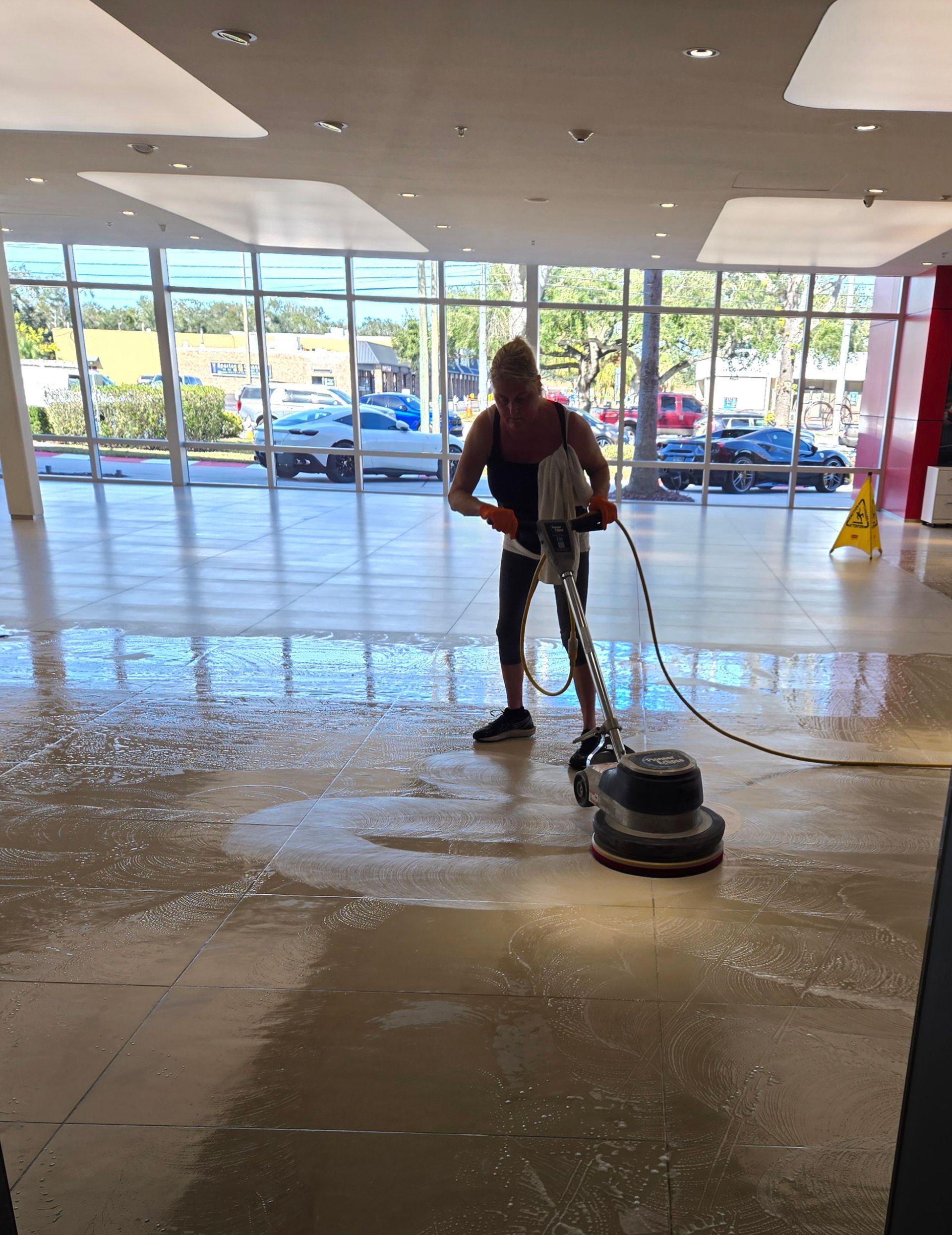 Worker using a floor scrubber in a bright storefront lobby near glass doors
