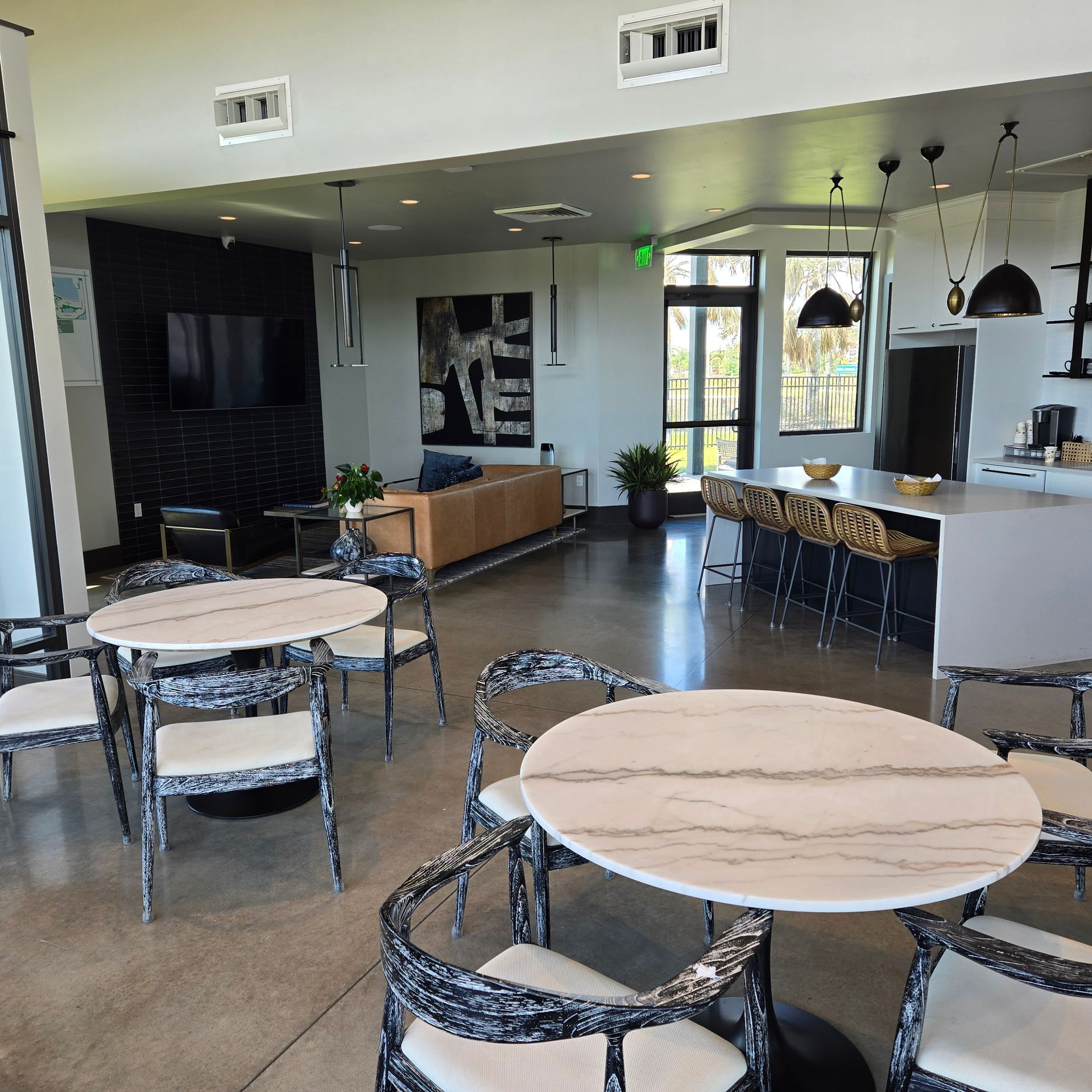 Modern café interior with round marble tables, metal chairs, and a bar seating area near large windows.