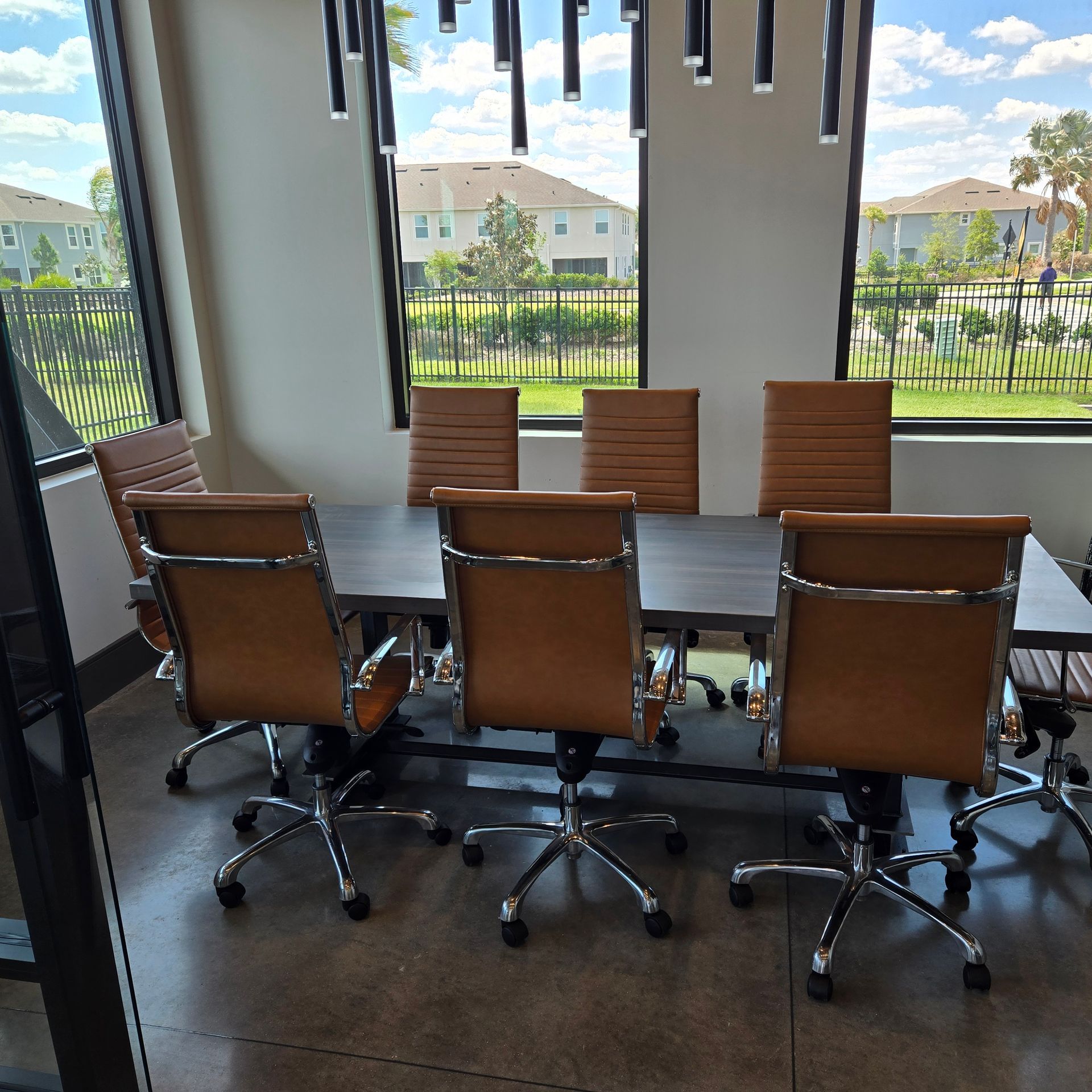 Conference room with dark table and brown swivel chairs by large windows overlooking a courtyard