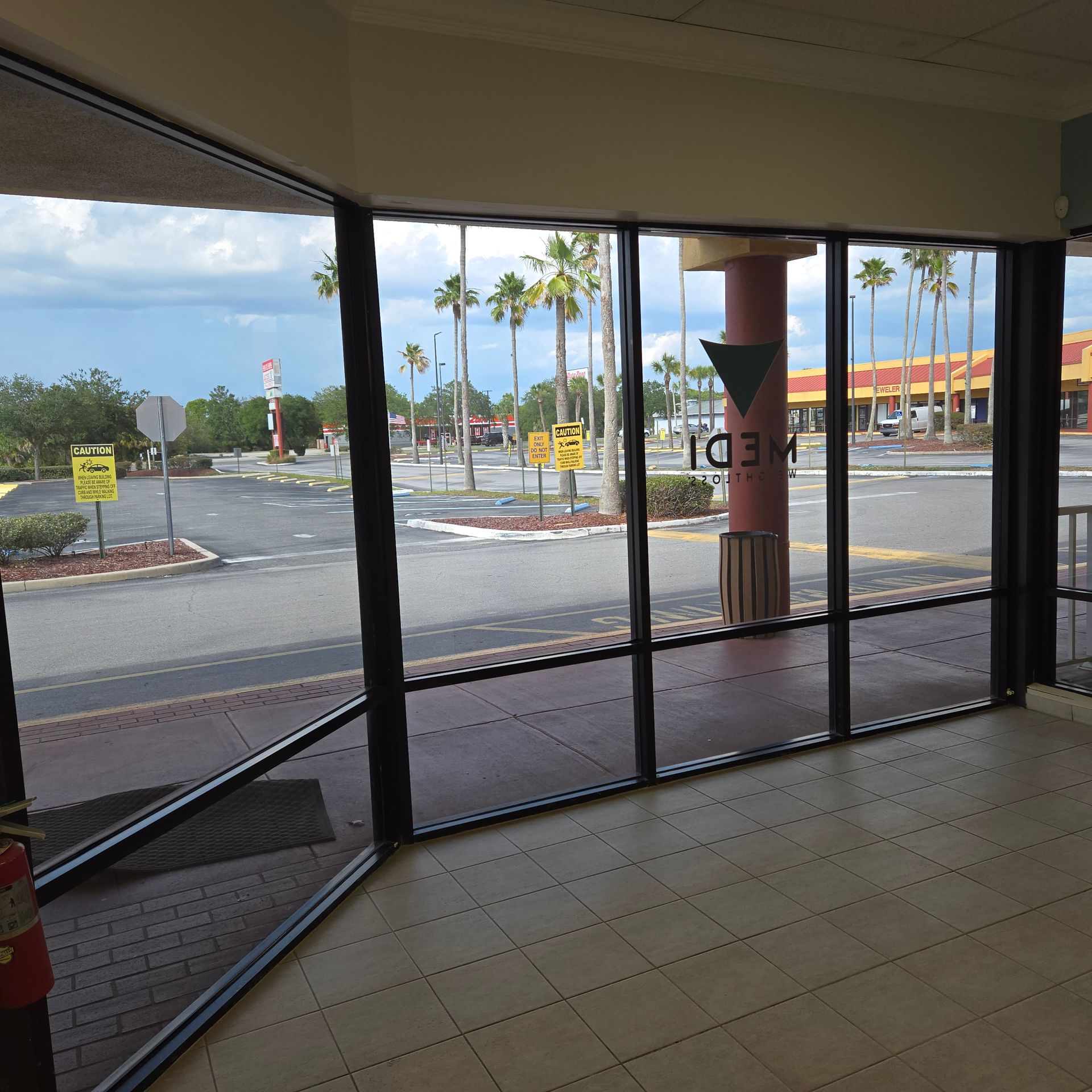 Empty storefront interior with glass doors overlooking a parking lot and palm trees outside