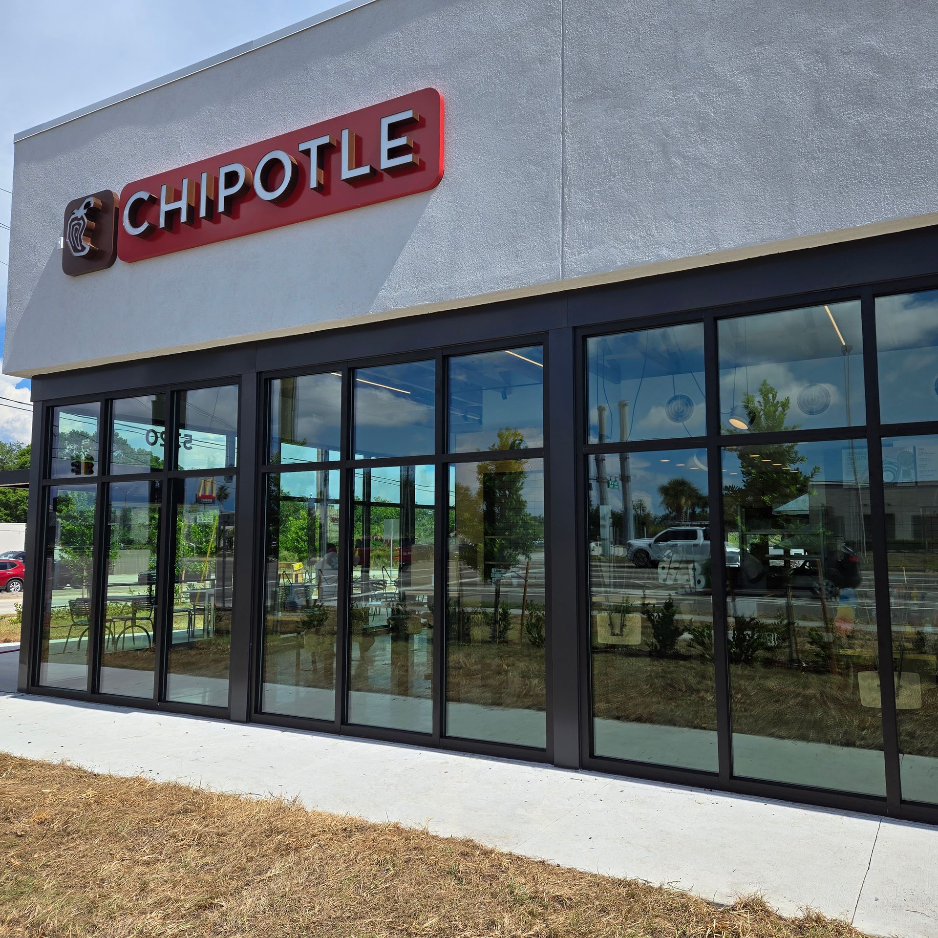 Chipotle storefront with red sign and large glass windows on a sunny day