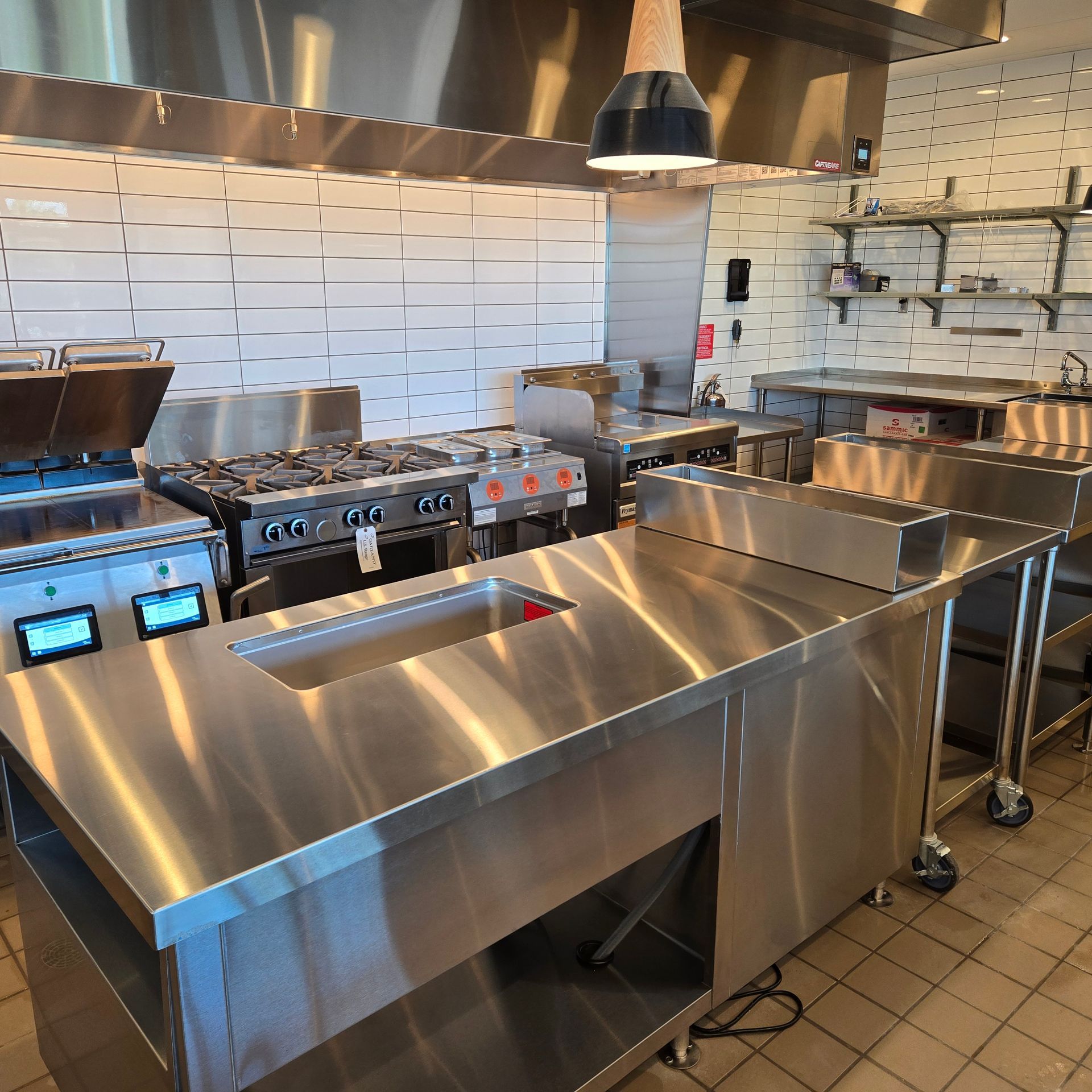 Stainless steel commercial kitchen with stovetops, griddles, ventilation hoods, and tiled walls