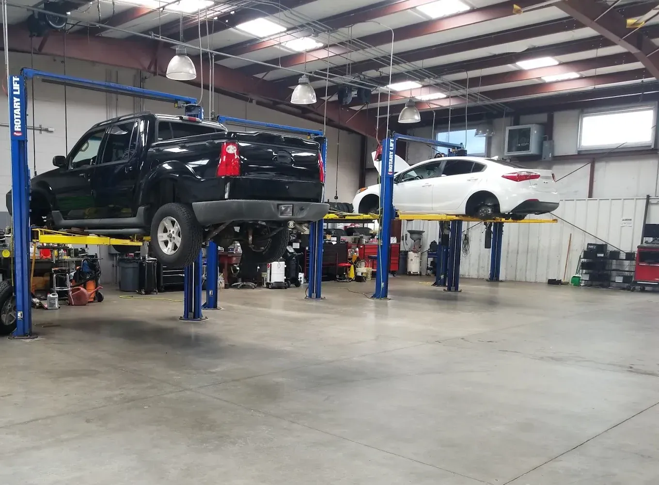 Auto repair shop with a black pickup on a lift and a white car in the background