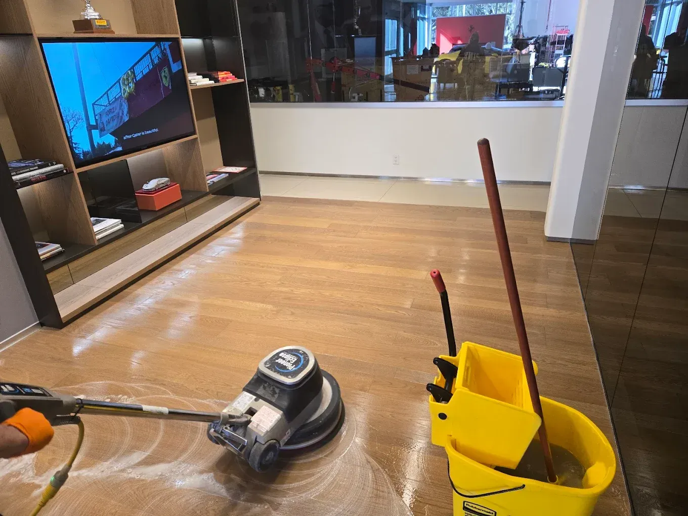 Vacuum cleaner and yellow mop bucket on a hardwood floor in a living room.