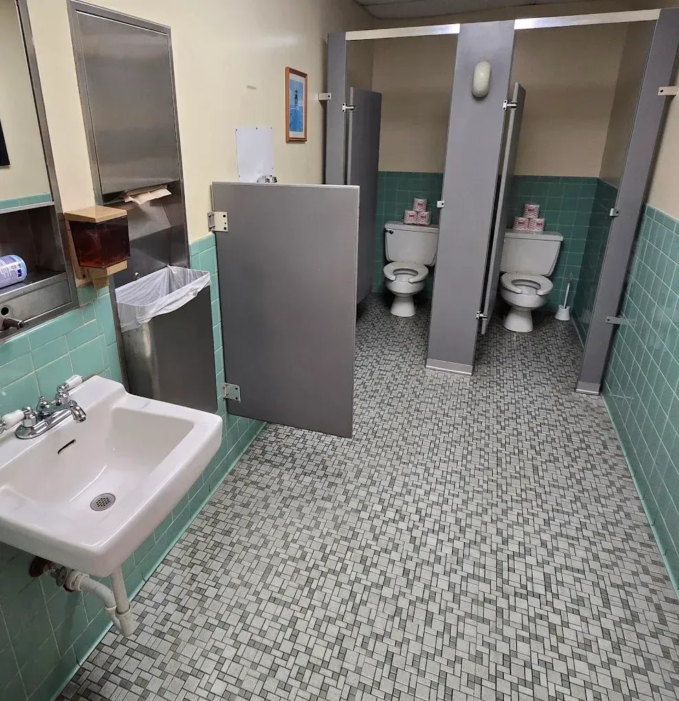 Public restroom with sinks, stalls, and patterned tile flooring, viewed from the entrance.