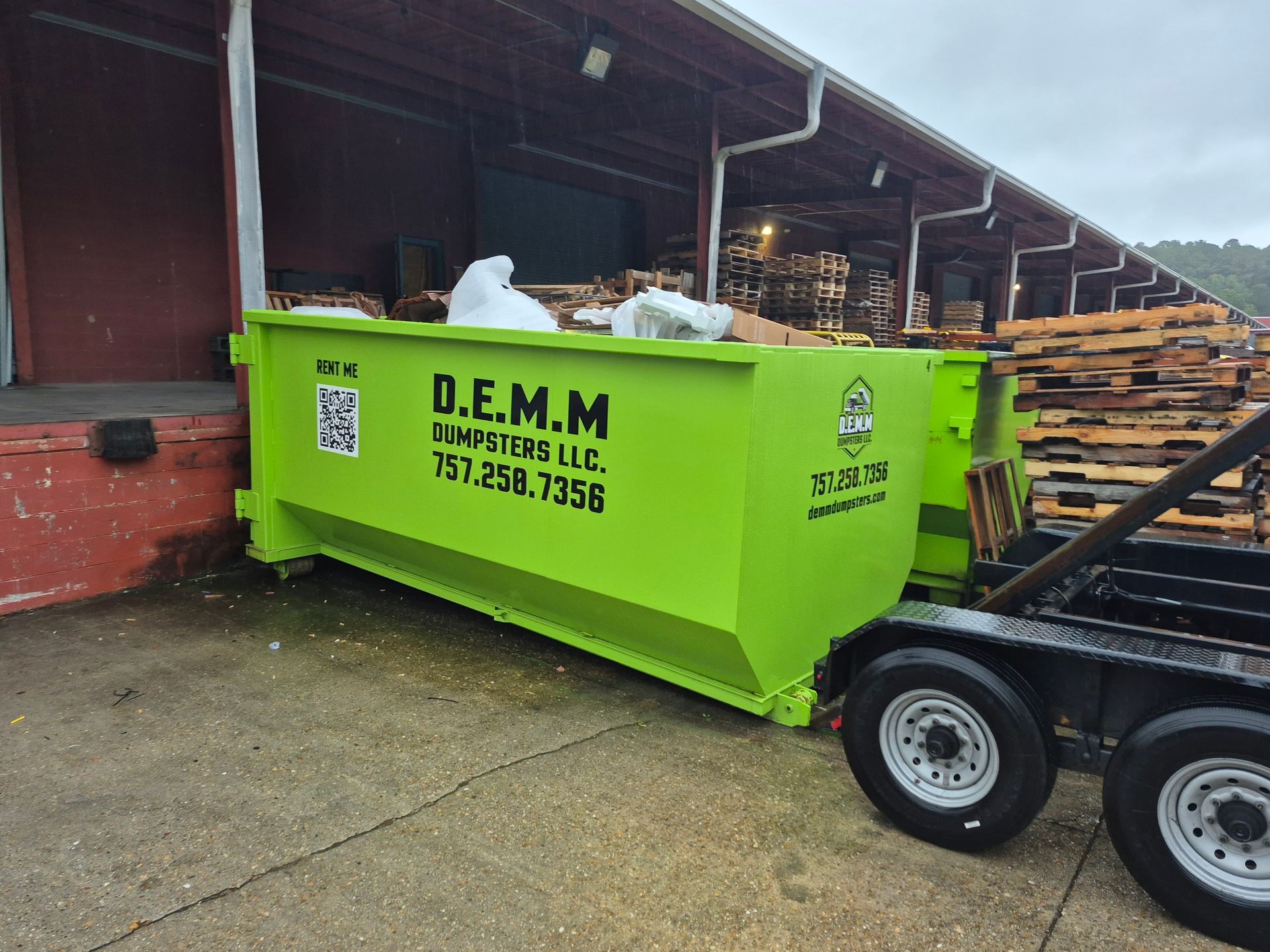 Two bright green dumpsters under a dark loading area, filled with wood and other construction debris.