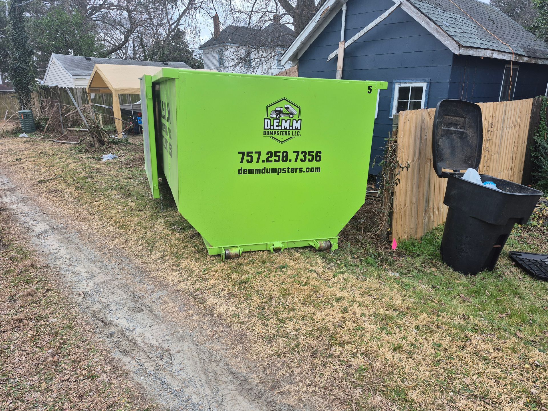 Two bright green industrial dumpsters stacked outdoors against a blue sky.