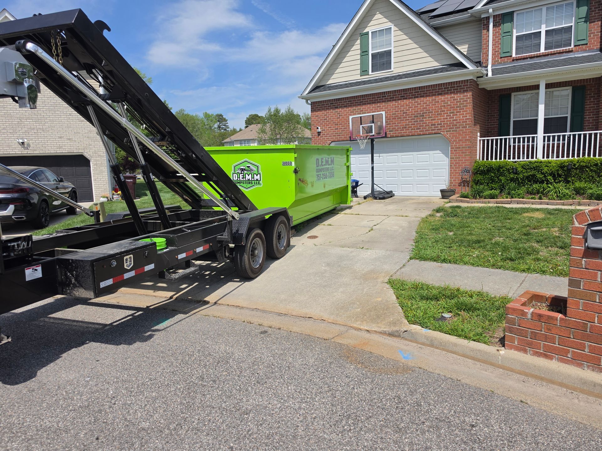 Two bright green dumpsters sit under a dark roof, with assorted wood and debris behind them.