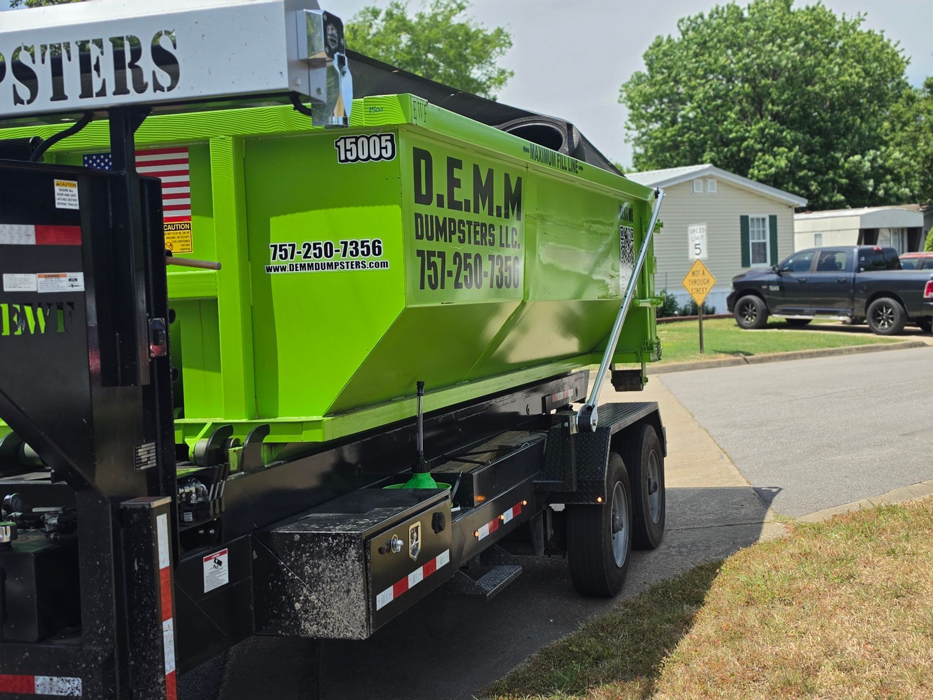 Bright green dumpster in an industrial setting, partially obscuring a cluttered background of wood and other materials.