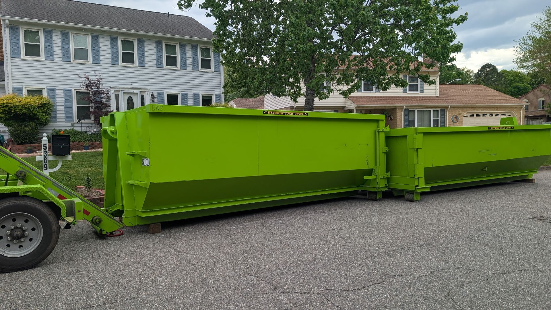 A bright green dumpster on a grassy lawn, angled, with a tree in the background.