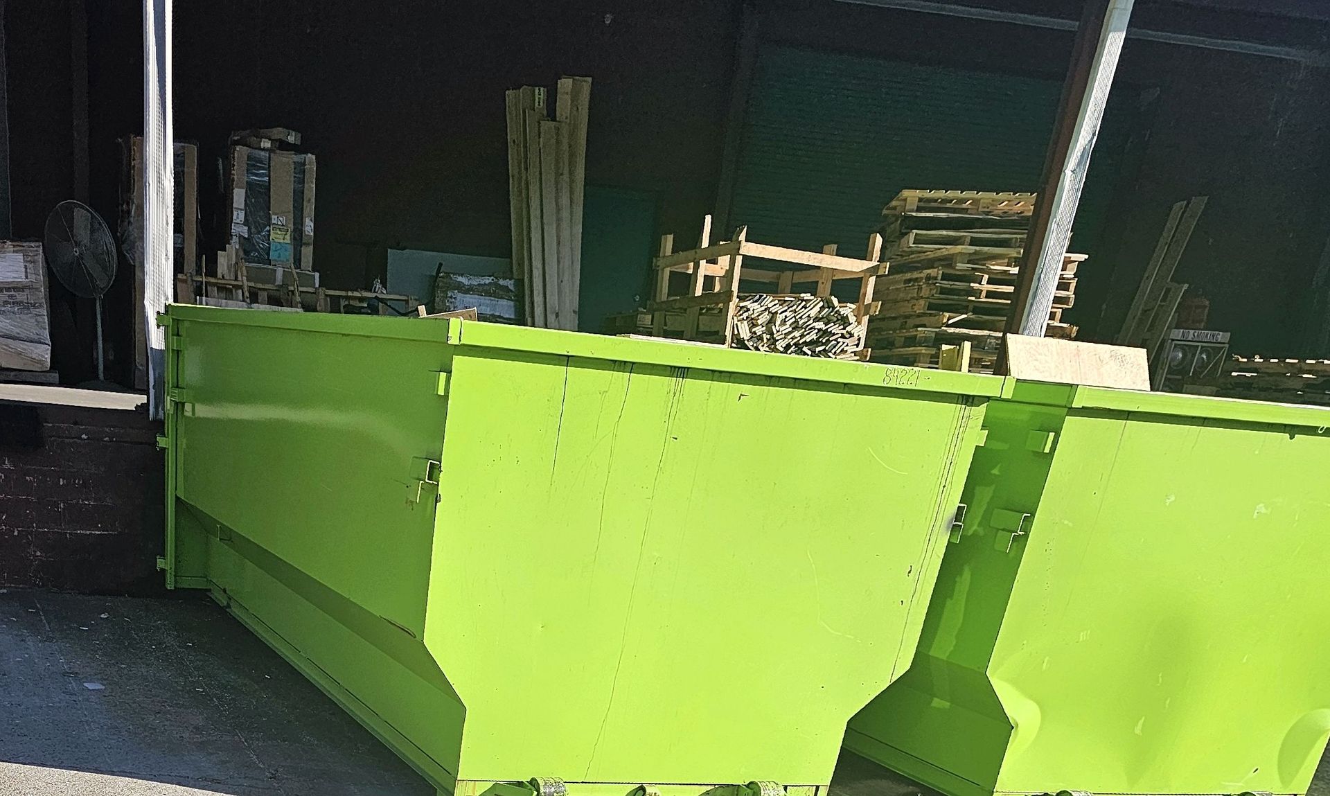 Lime green dumpster outdoors near stacks of wood.