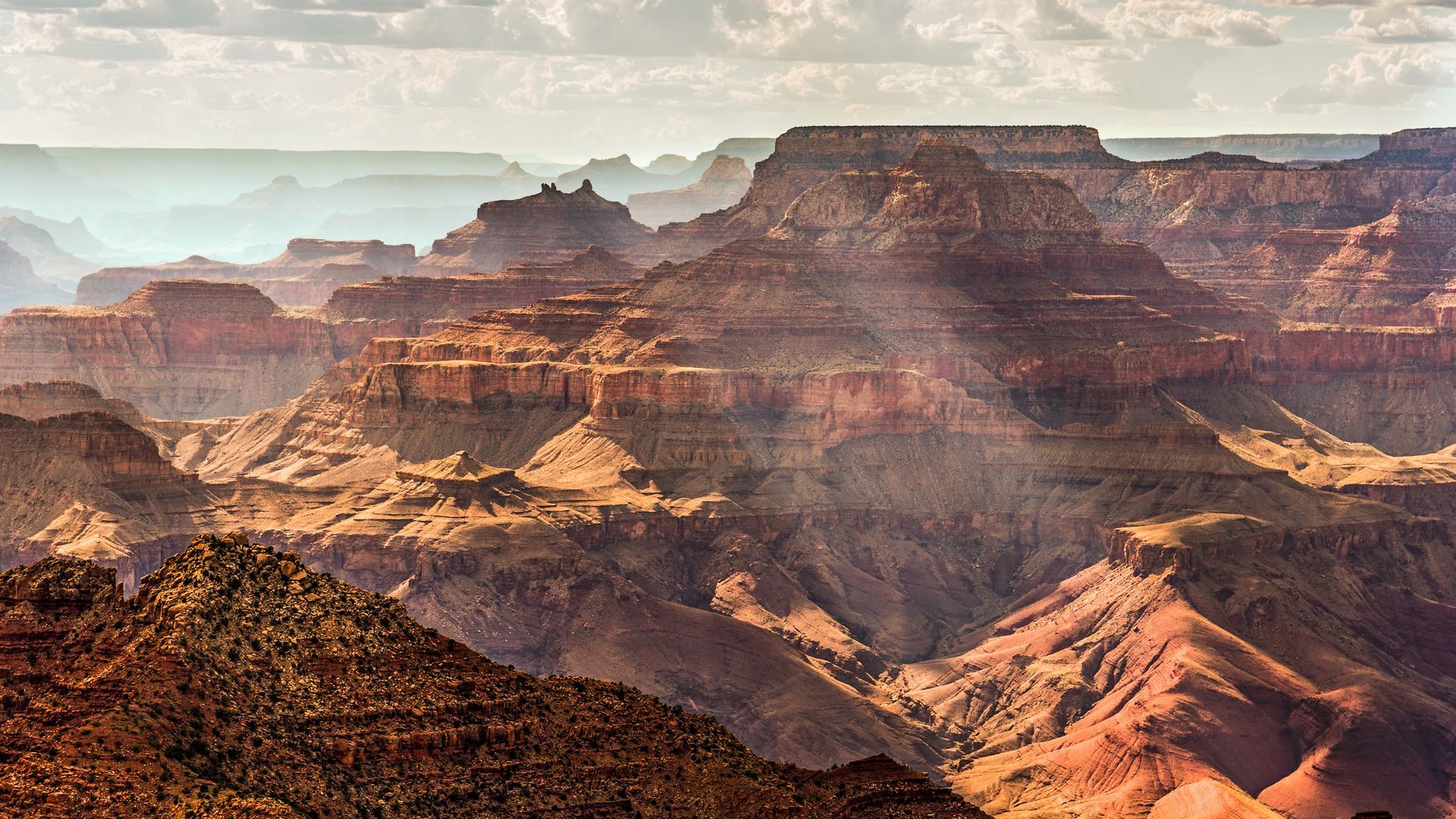 Sunlit layered red rock canyon with mesas and hazy cliffs under a pale sky