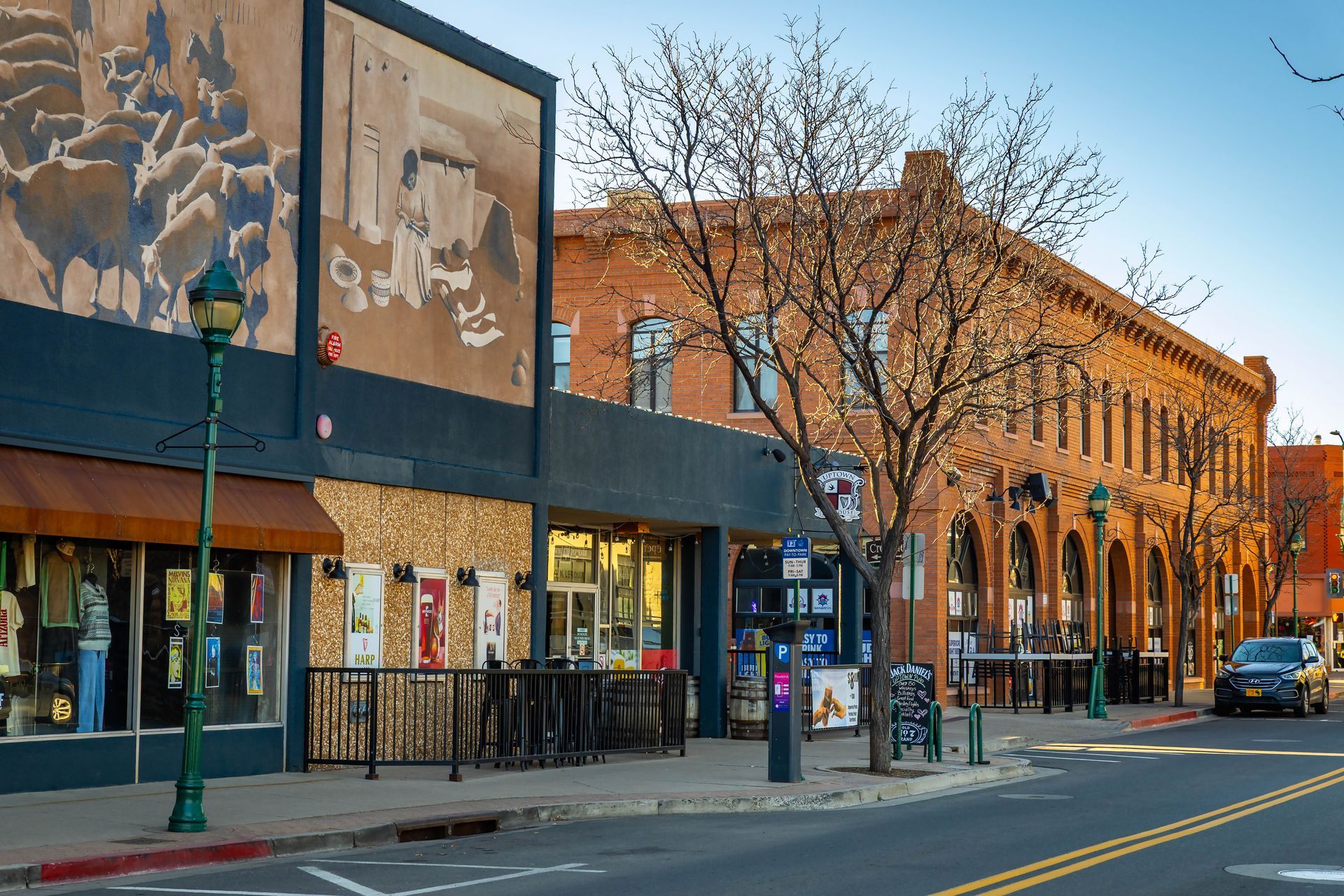 Small-town street with storefronts, murals, bare trees, and parked cars at sunset