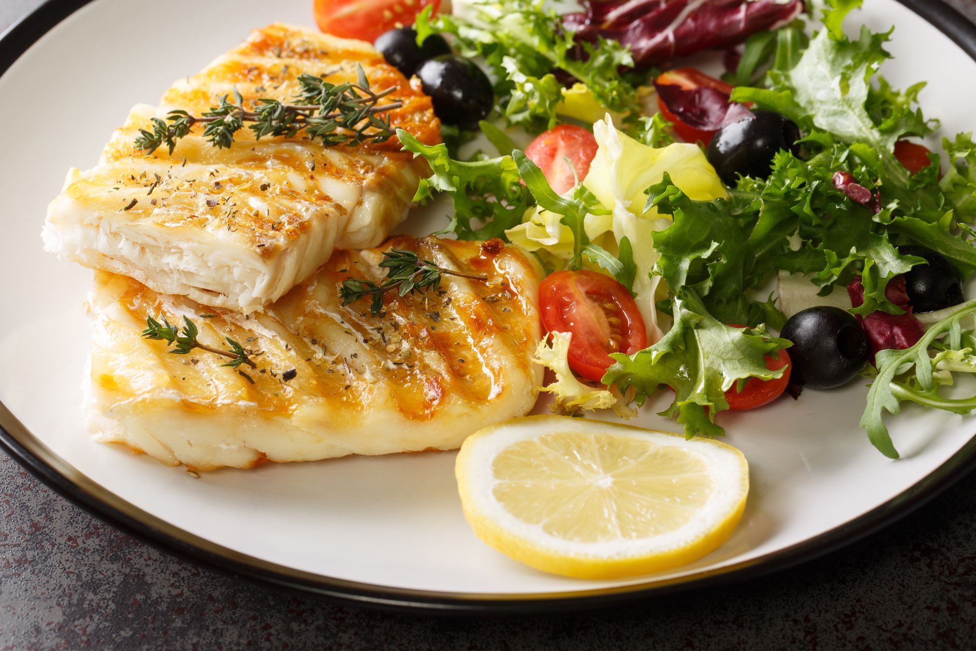 Grilled fish fillets with herbs, lemon wedge, and mixed green salad on a white plate