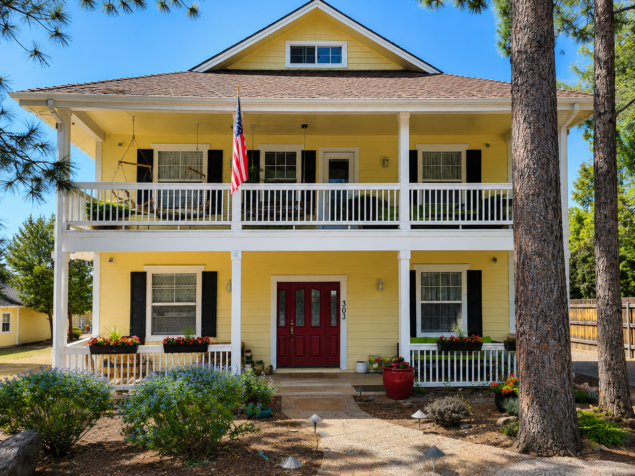 Yellow two-story house with white balcony, red front doors, and trees in the yard