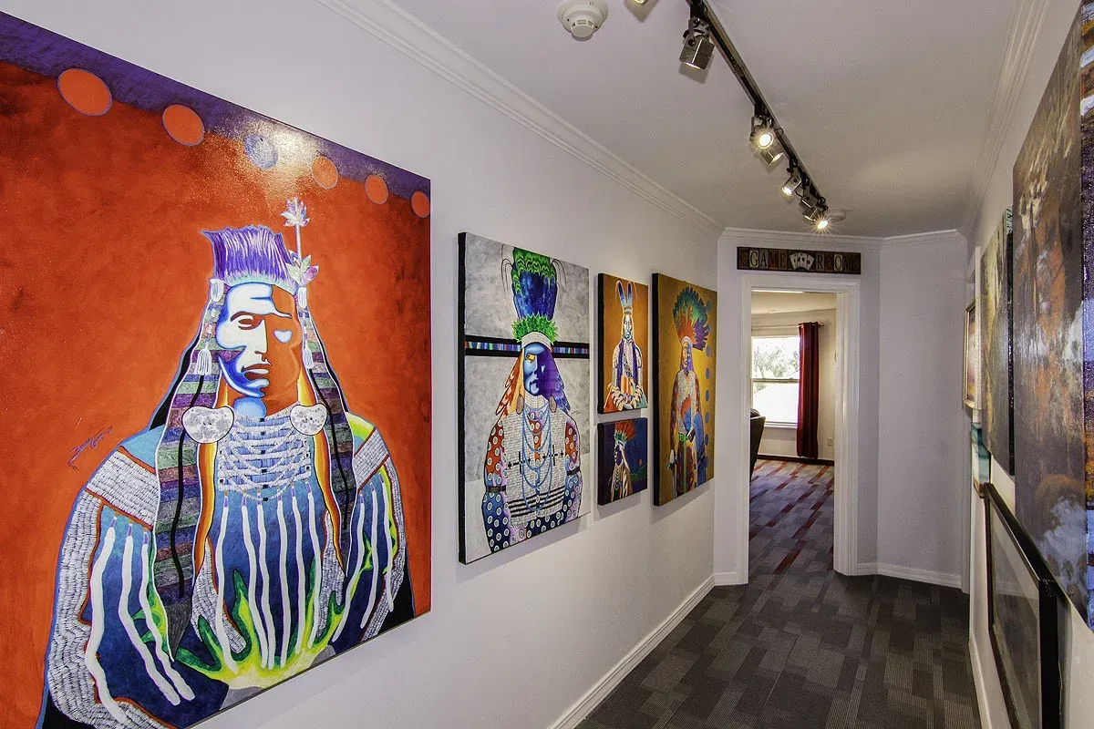 Art gallery hallway with colorful abstract paintings on white walls and dark wood flooring
