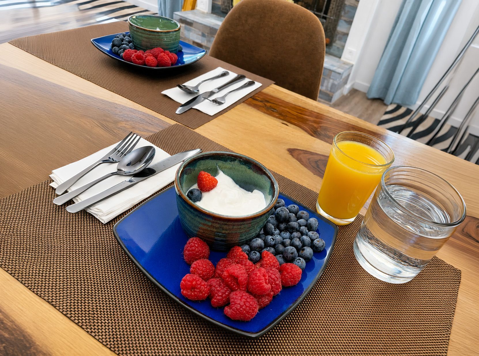Breakfast table with fruit, yogurt, orange juice, water, and neatly set silverware