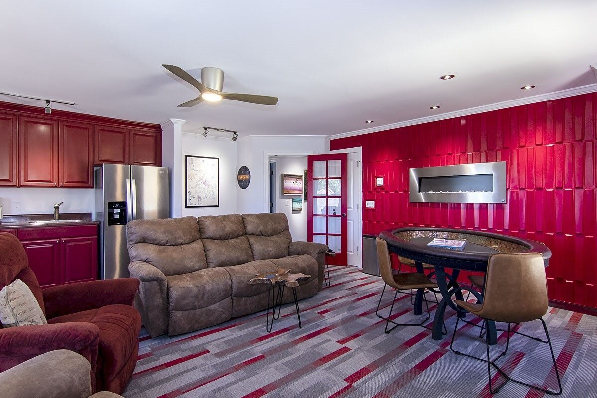 Living room with red walls, brown sofas, patterned carpet, dining table, and ceiling fan