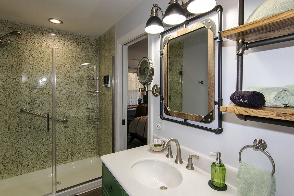 Bathroom with tiled shower, vanity sink, mirror, and wall shelves with decor and toiletries