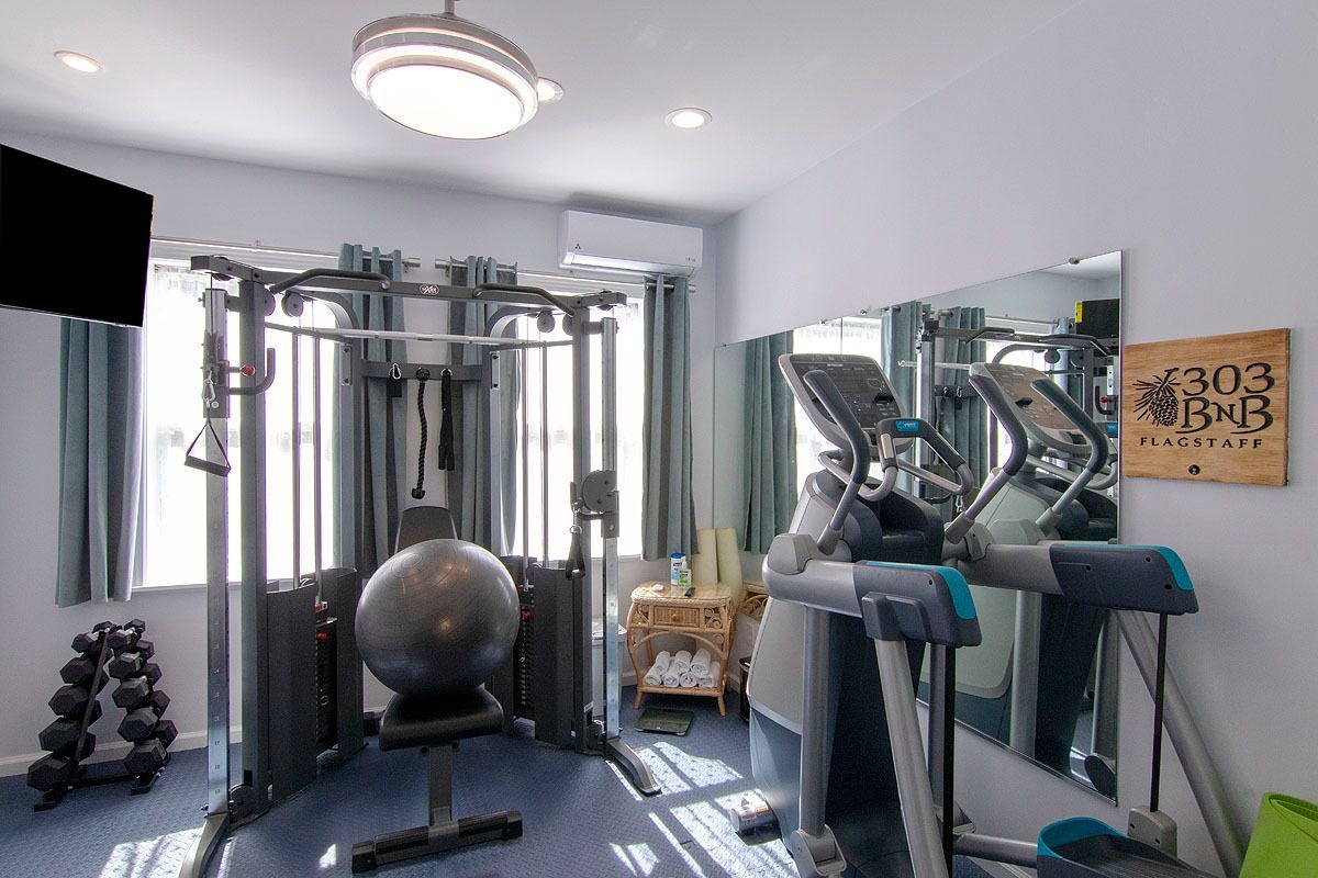 Home gym with weight machine, treadmill, exercise ball, dumbbells, and mirror on a bright white room.