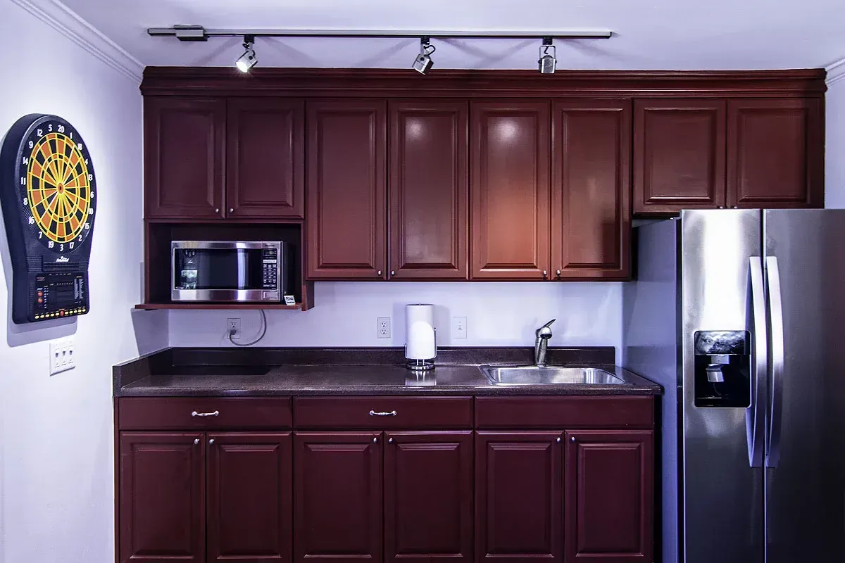 Small kitchen with dark wood cabinets, black countertop, stainless fridge, and wall clock.