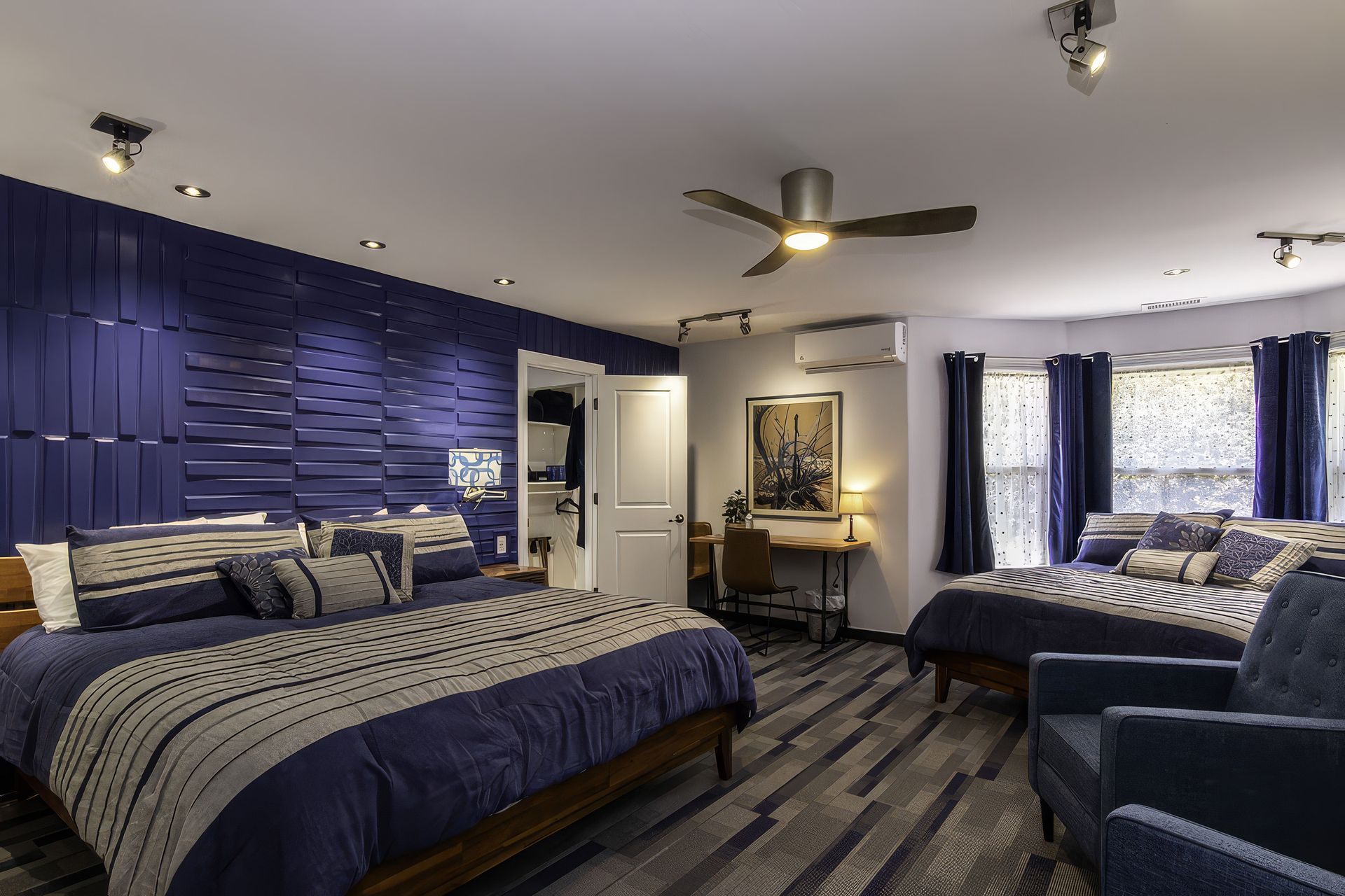 Spacious modern bedroom with two beds, blue accent wall, ceiling fan, and patterned carpet.
