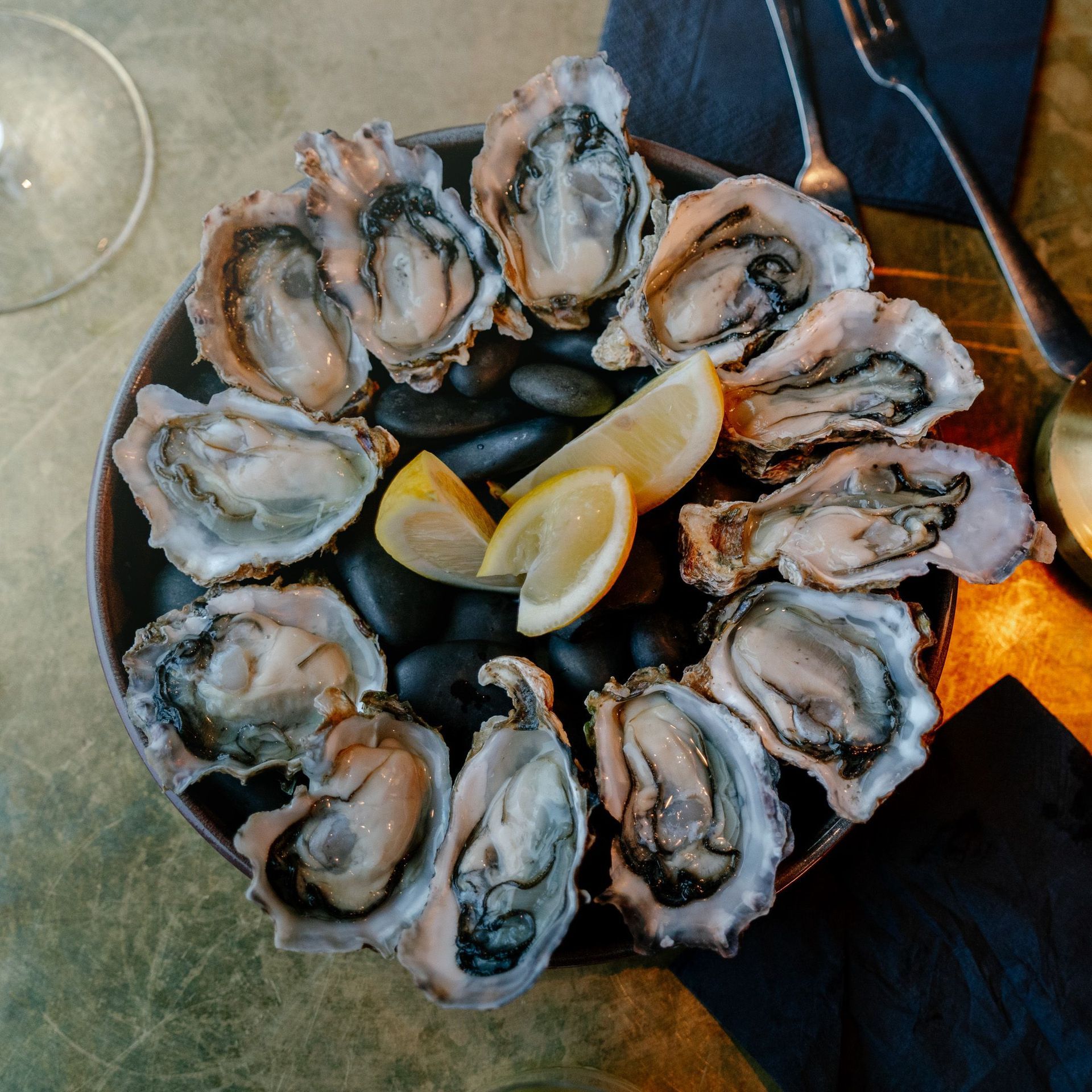 Plate of raw oysters on ice with lemon wedges on a dark table
