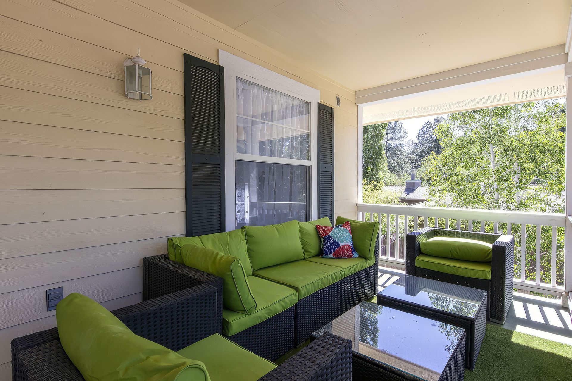 Green patio seating on a covered porch with a glass coffee table and outdoor view