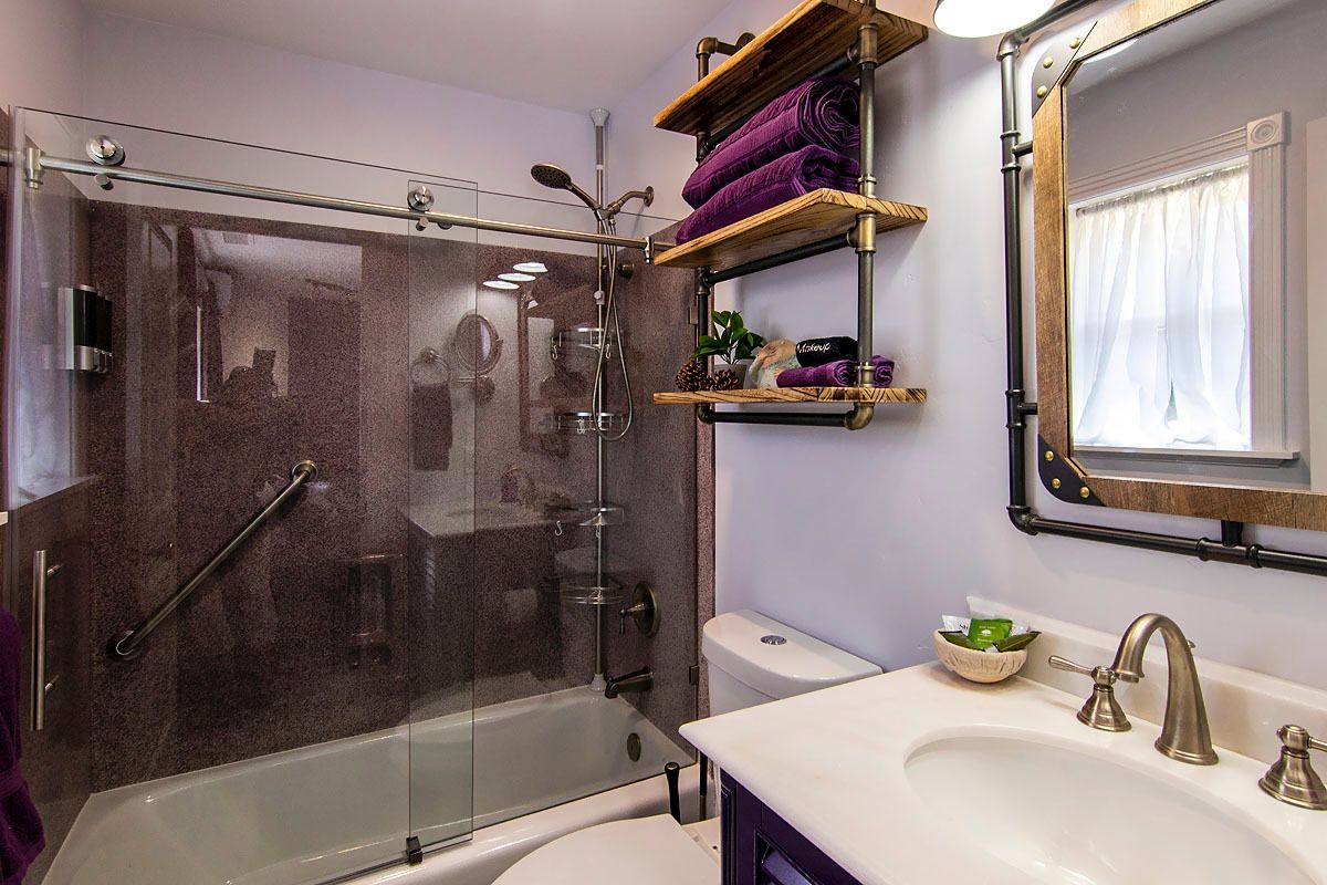 Bathroom with glass shower, white sink, purple walls, and towel shelves by a window