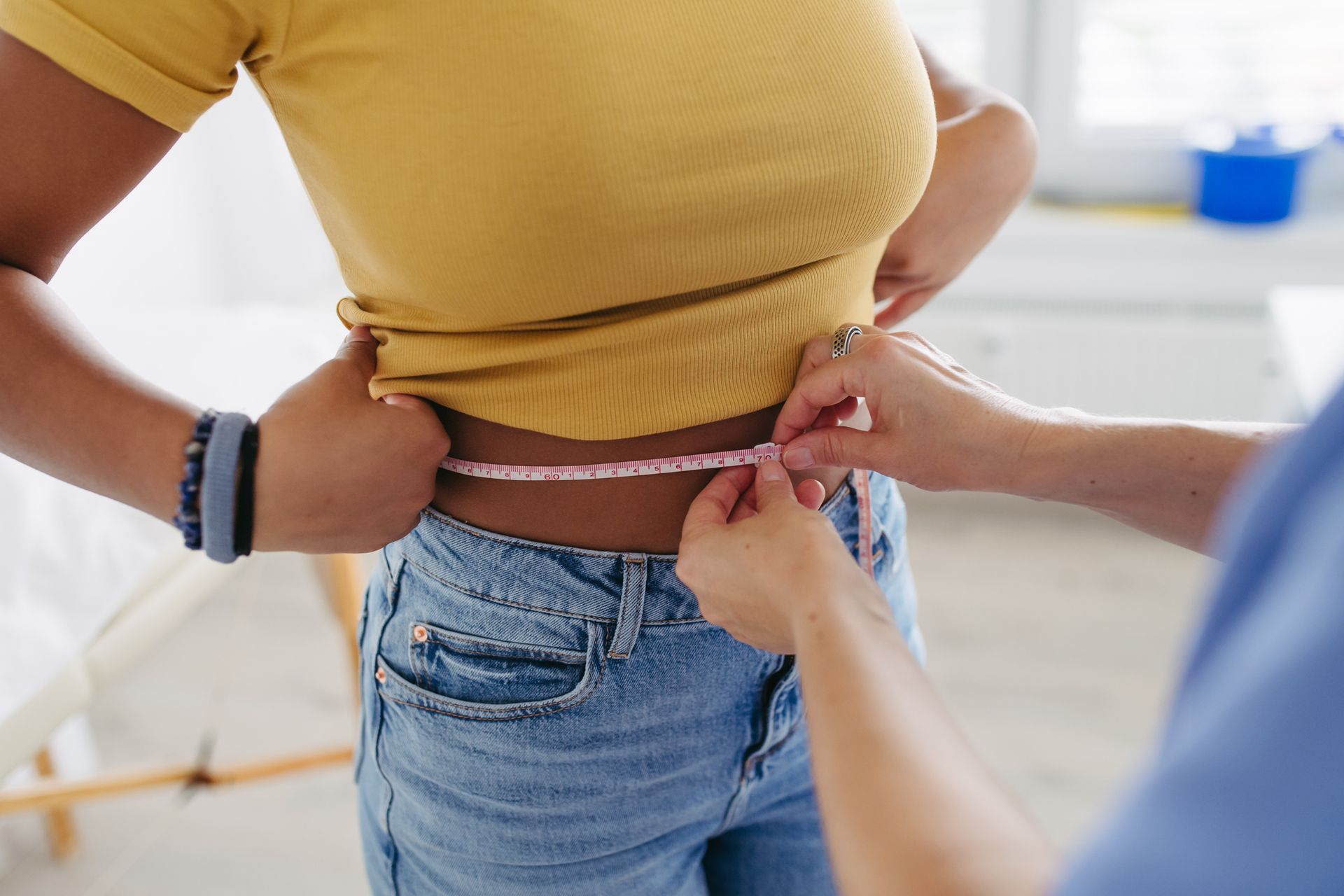 Person measuring waist with tape measure to track weight loss progress.
