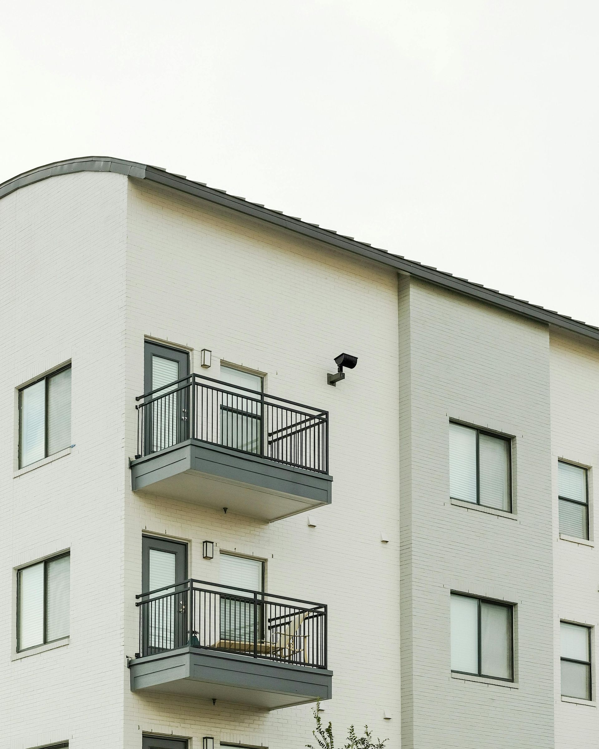 A light-colored multi-story apartment building with a curved corner, balconies, and rectangular windows.