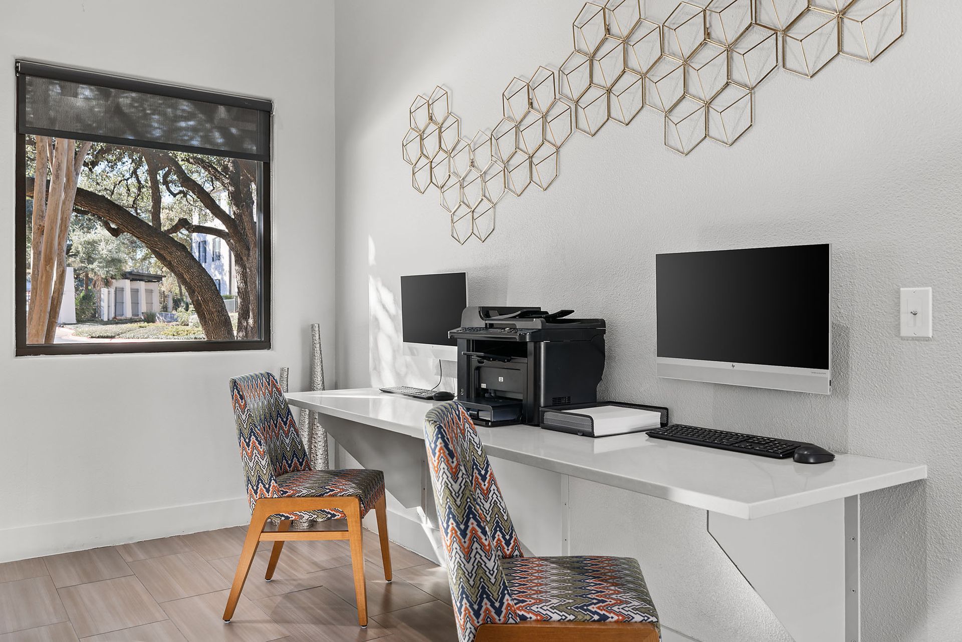 Modern home office with two desks, monitors, printer, patterned chairs, and a wall art display at Marquis at Great Hills in Austin, TX.
