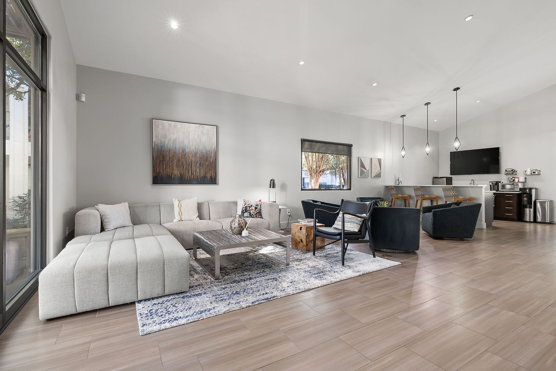 Open-concept living room with gray sectional, coffee table, dining area, and kitchen in neutral tones at Marquis at Great Hills in Austin, TX.