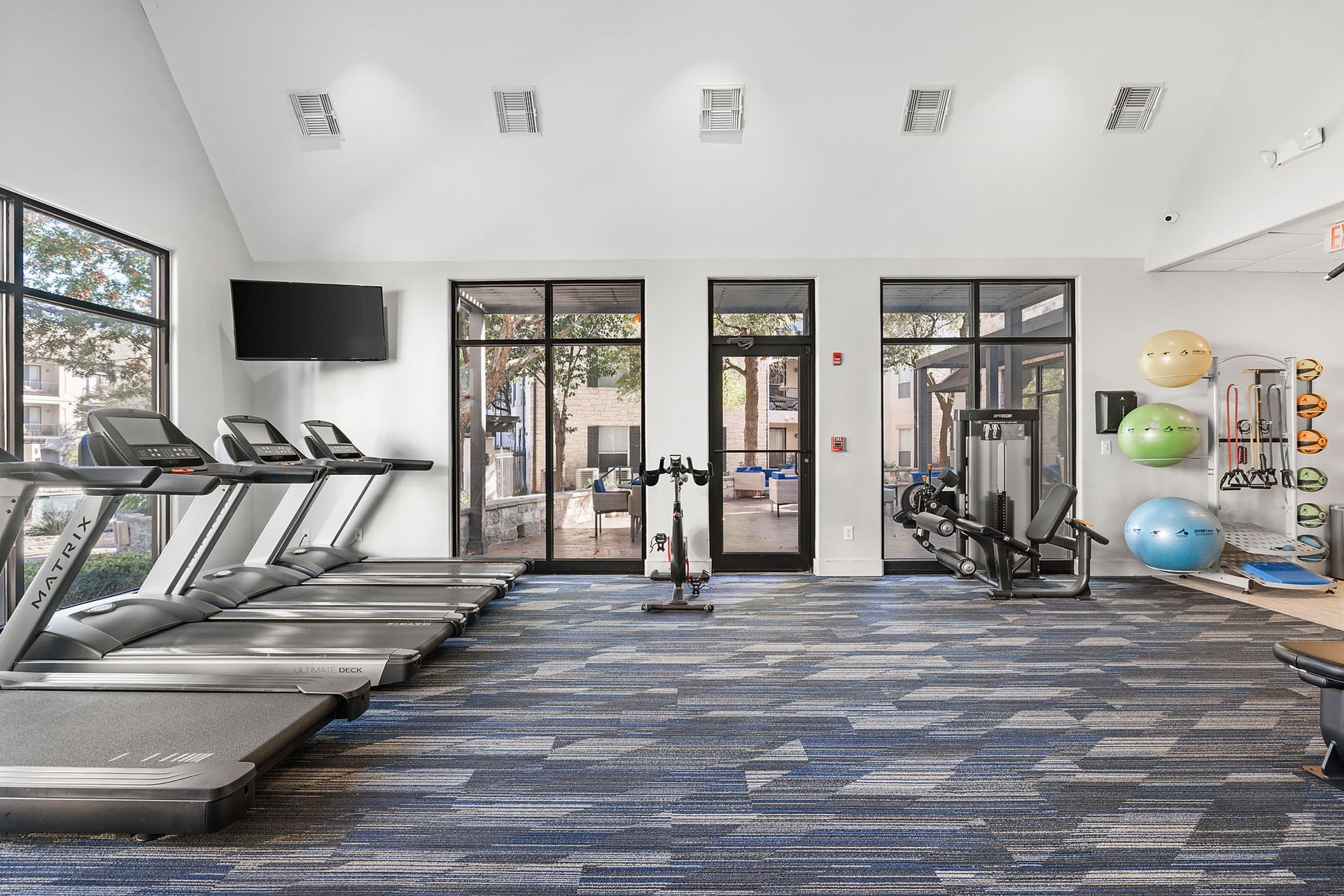 Modern gym interior with treadmills, exercise machines, weights, and blue stability balls at Marquis at Great Hills in Austin, TX.