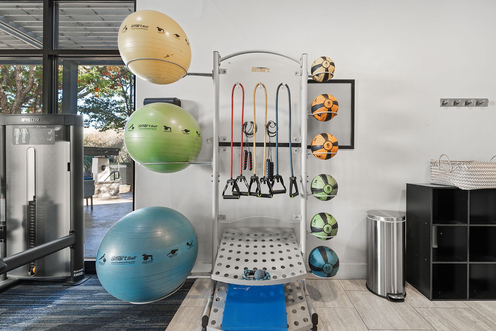 Gym workout area with colorful stability balls and hanging resistance bands by a cable machine at Marquis at Great Hills in Austin, TX.