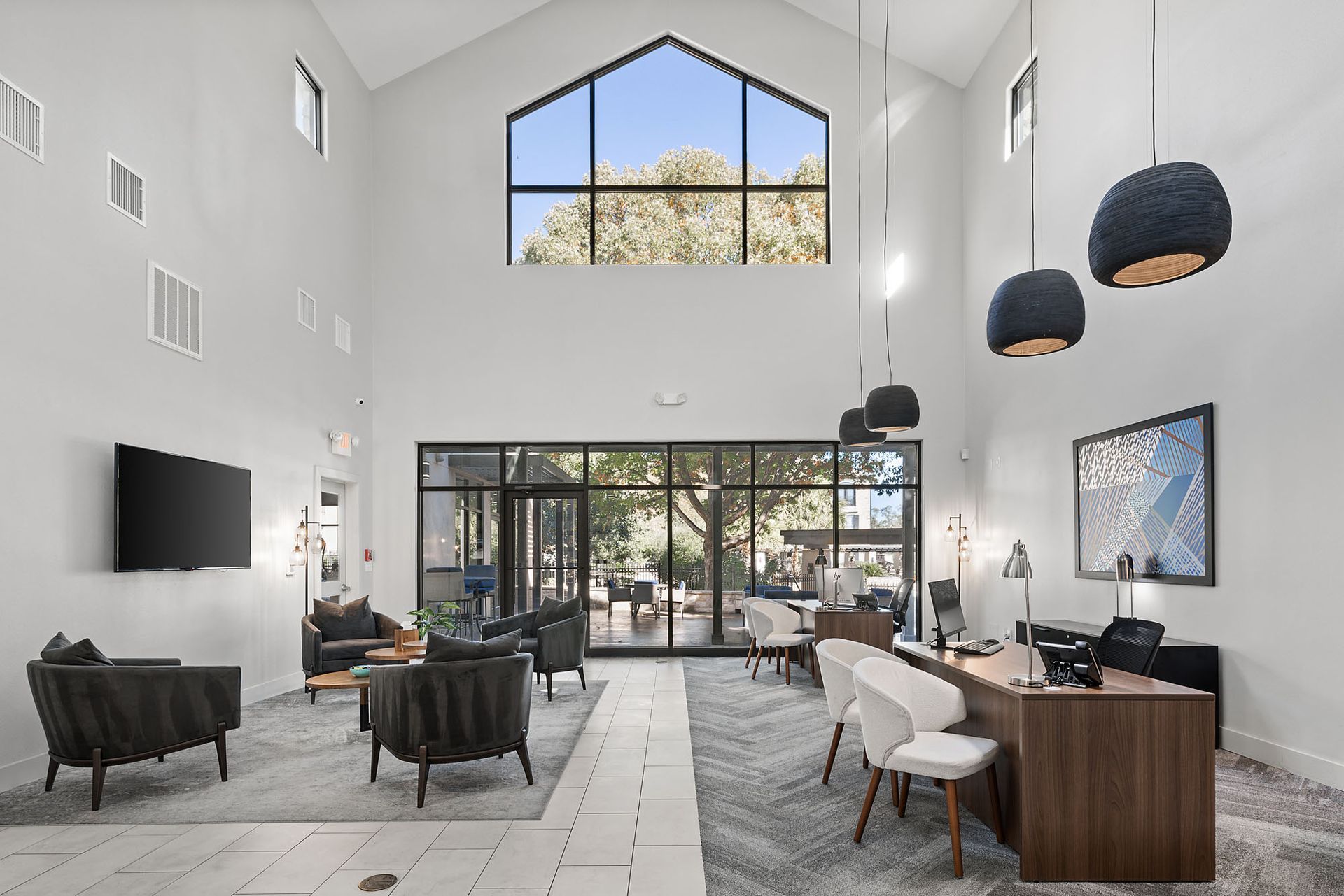 Bright modern lobby with high ceiling, glass doors, black chairs, and desks in a spacious white interior at Marquis at Great Hills in Austin, TX.