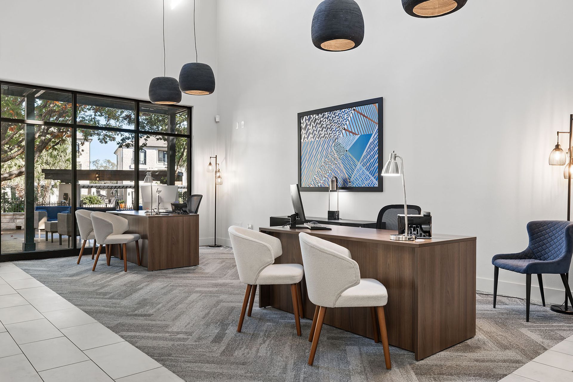 Modern office reception area with wood desks, blue chairs, pendant lights, and a large framed artwork at Marquis at Great Hills in Austin, TX.