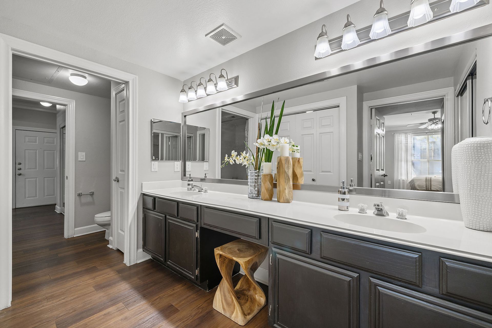 Modern bathroom with double vanity, large mirrors, white countertops, and dark cabinets; hallway visible through open door at Marquis at Great Hills in Austin, TX.