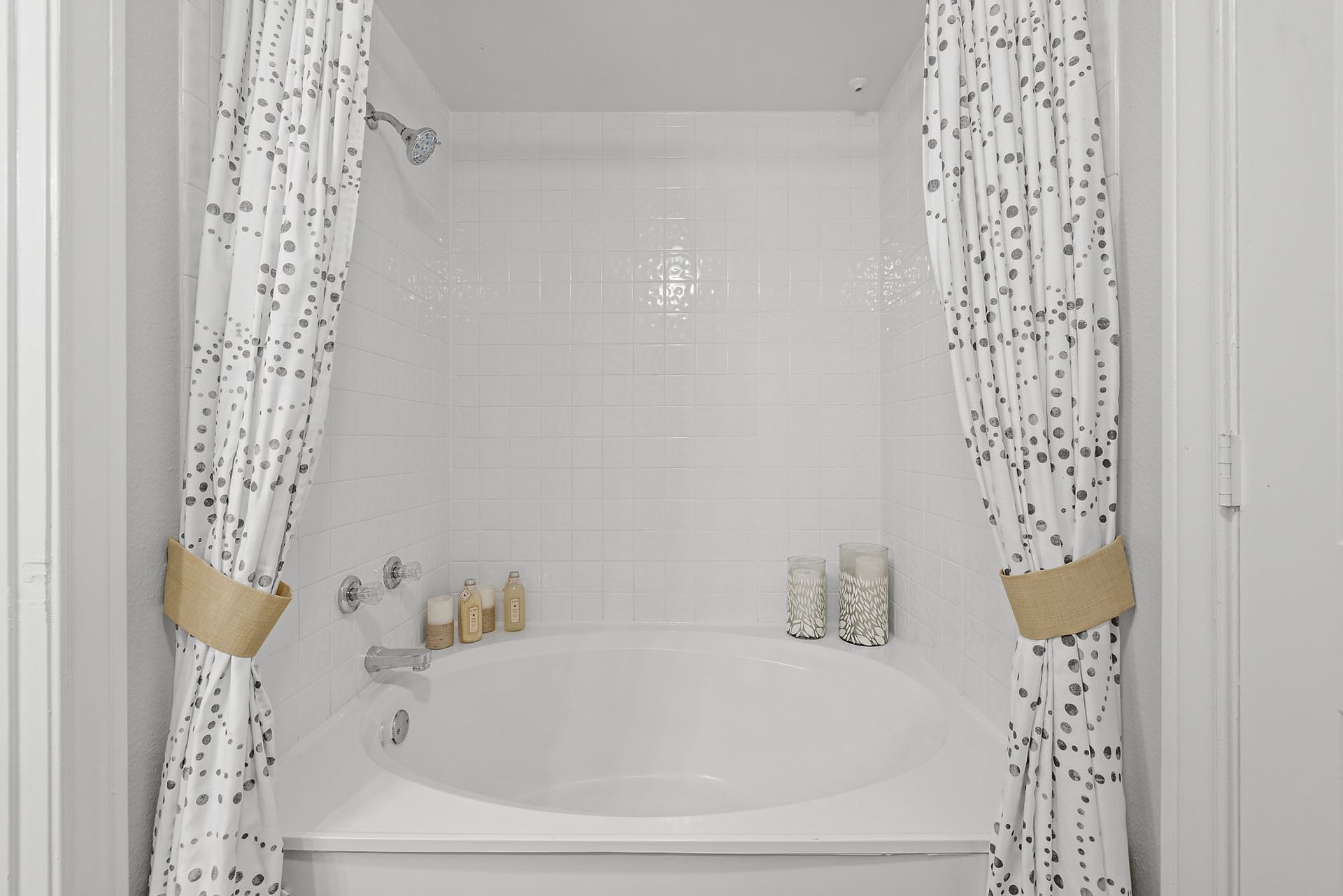 White bathroom with a bathtub, tiled shower wall, and patterned curtains tied back with gold bands at Marquis at Great Hills in Austin, TX.